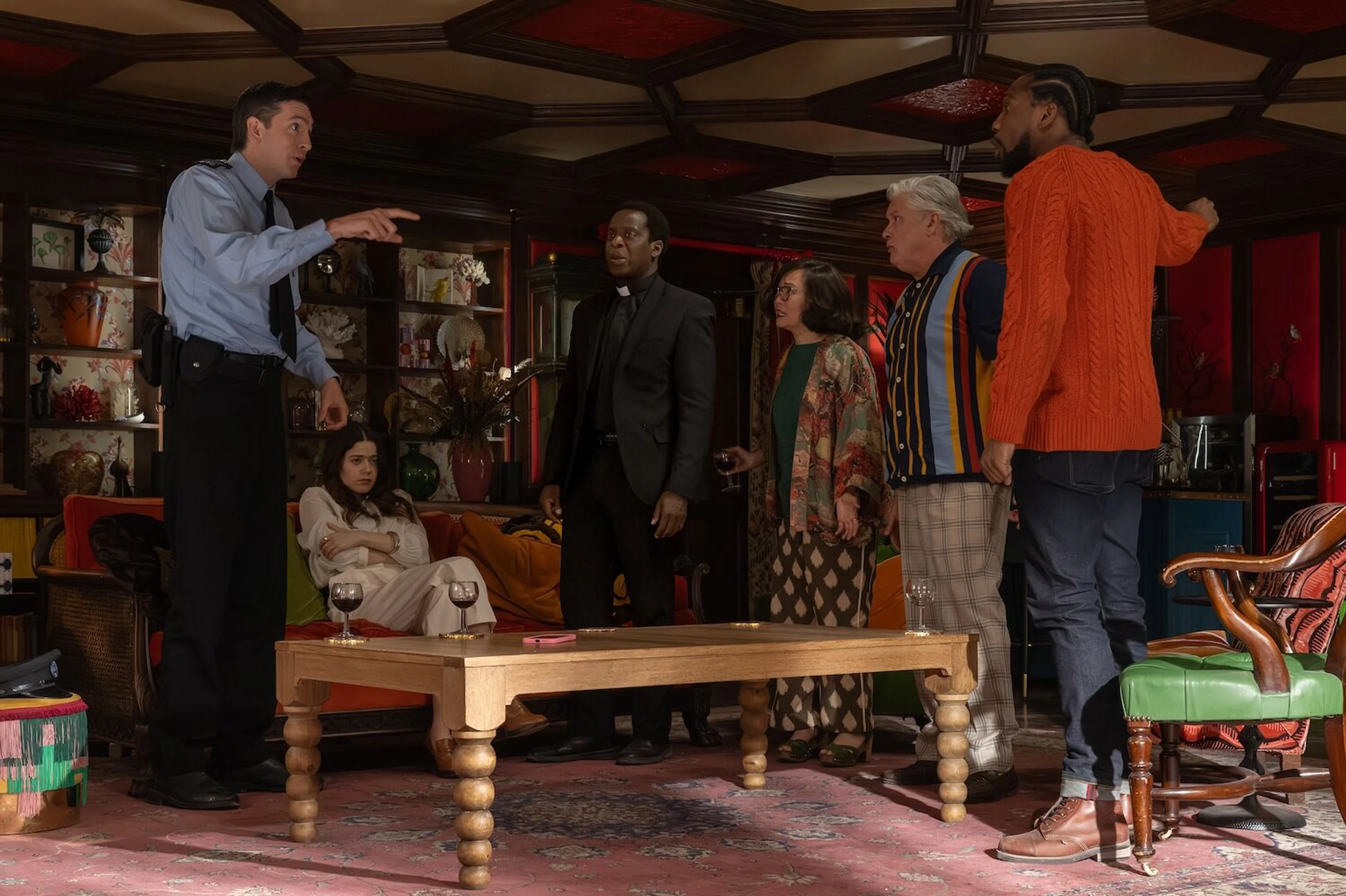 Several people gather around a table while a man on the left points across the room.
