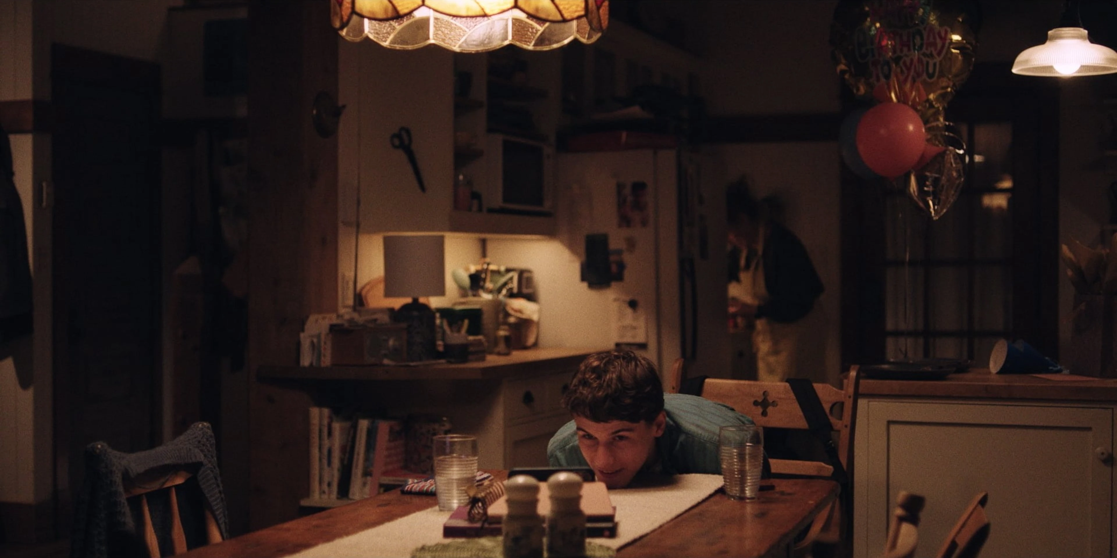 Sam Nivola peeks over a birthday table in a still from Hulu’s Phony press gallery.
