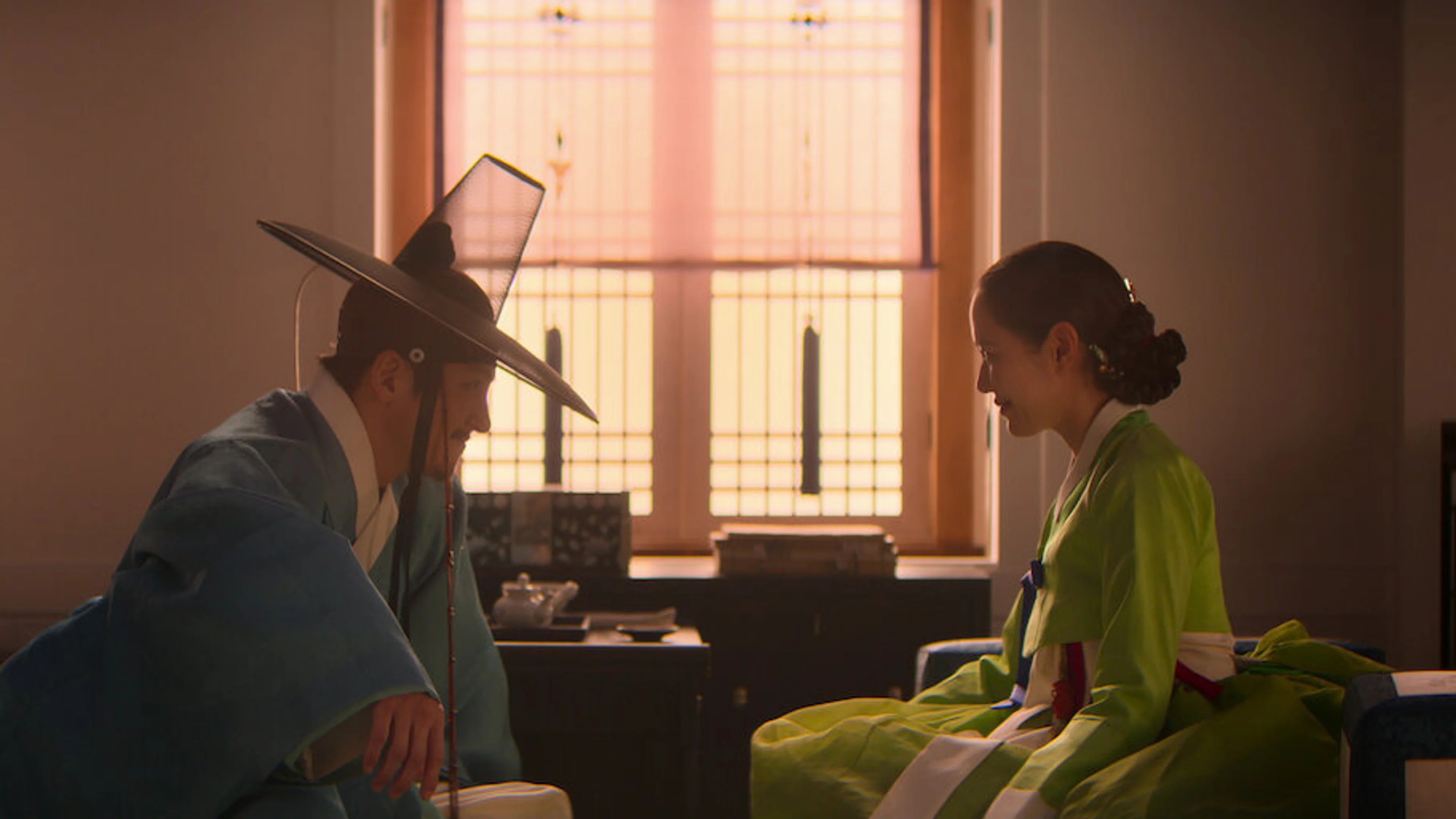 Two characters in Joseon-era clothing sit facing one another in a warmly lit room.