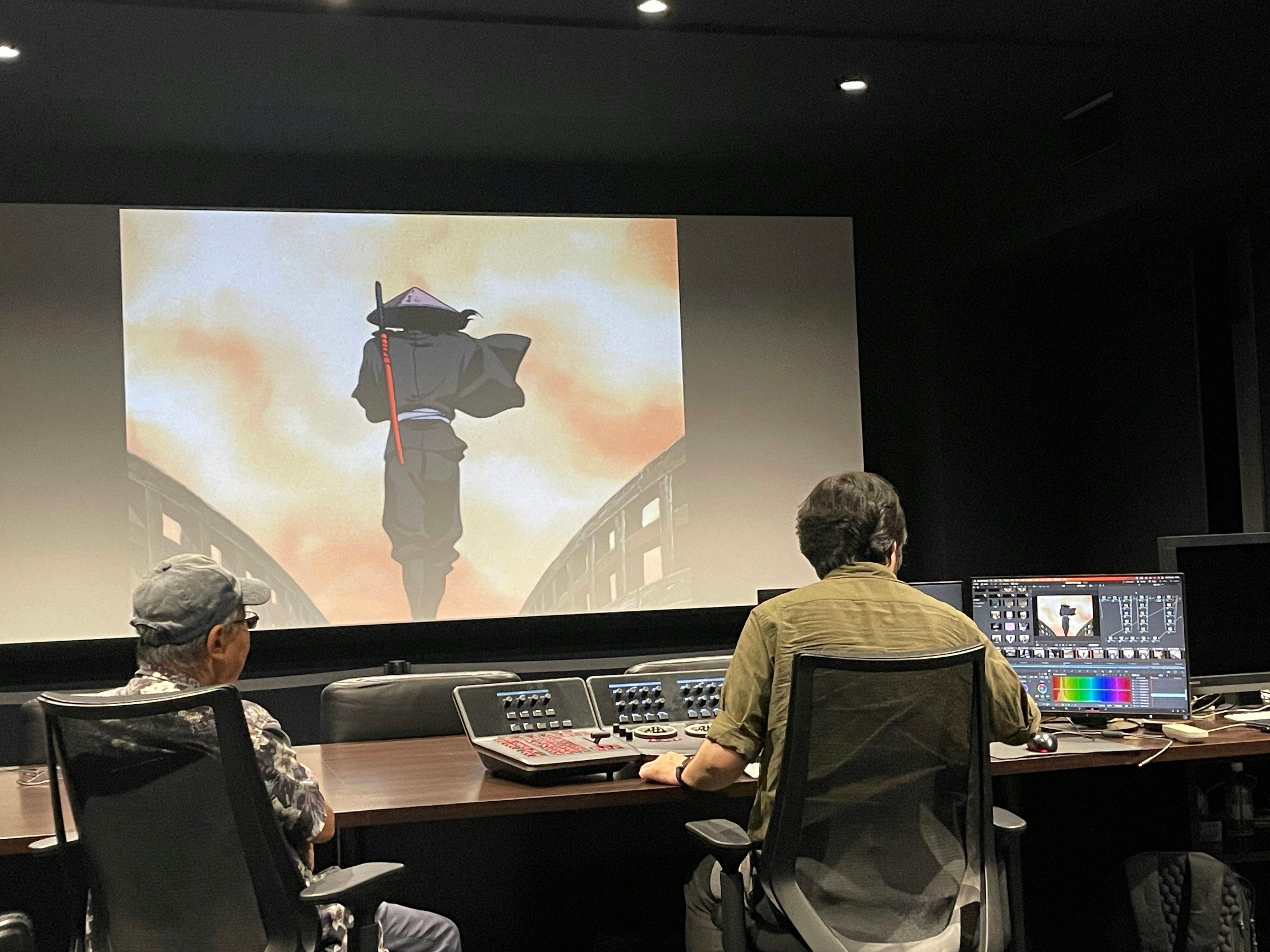 Two people watch Jubei projected on a large screen beside a color-correction monitor and control desk.