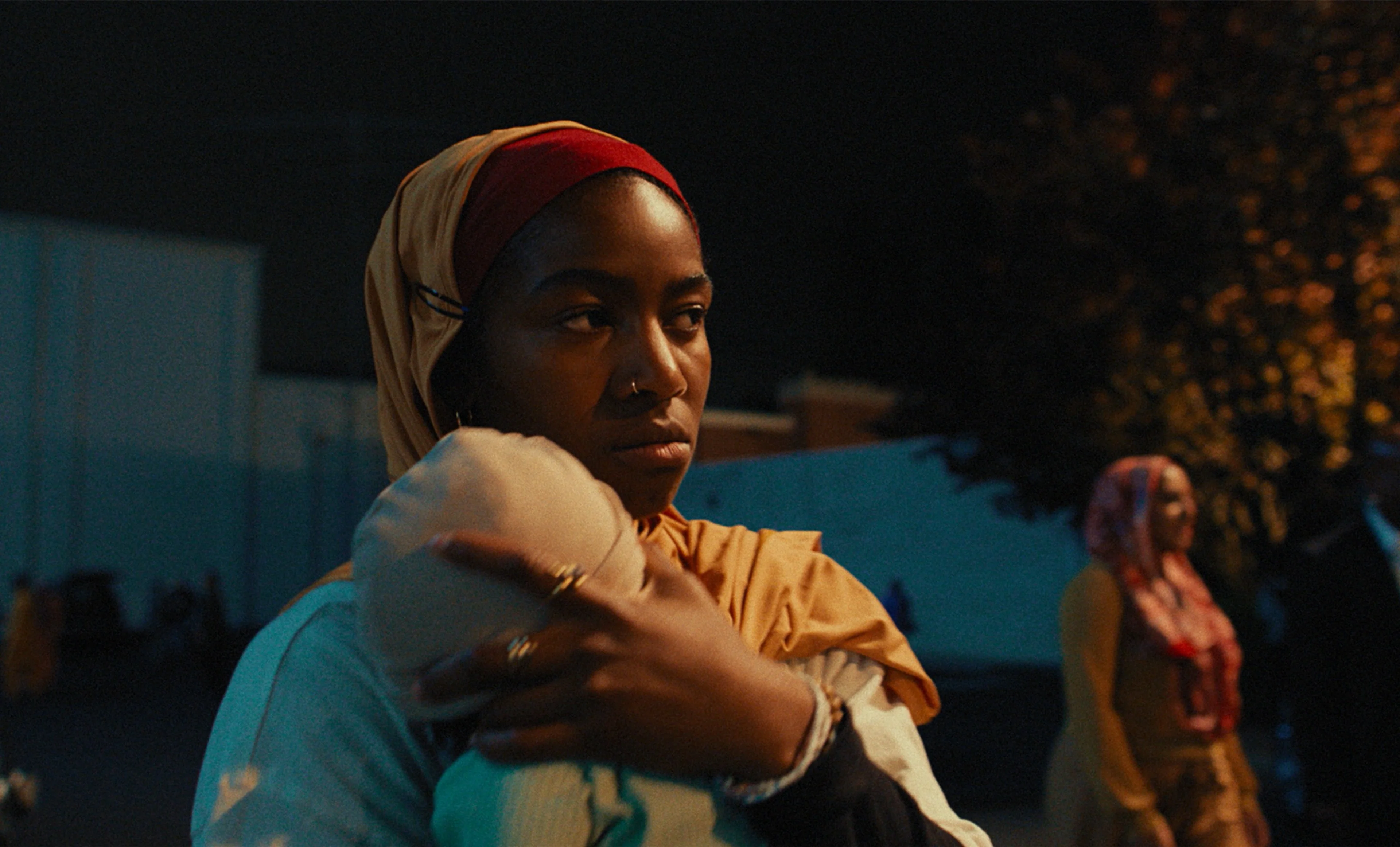Adia as Fatiha holds the family’s baby outdoors at night.