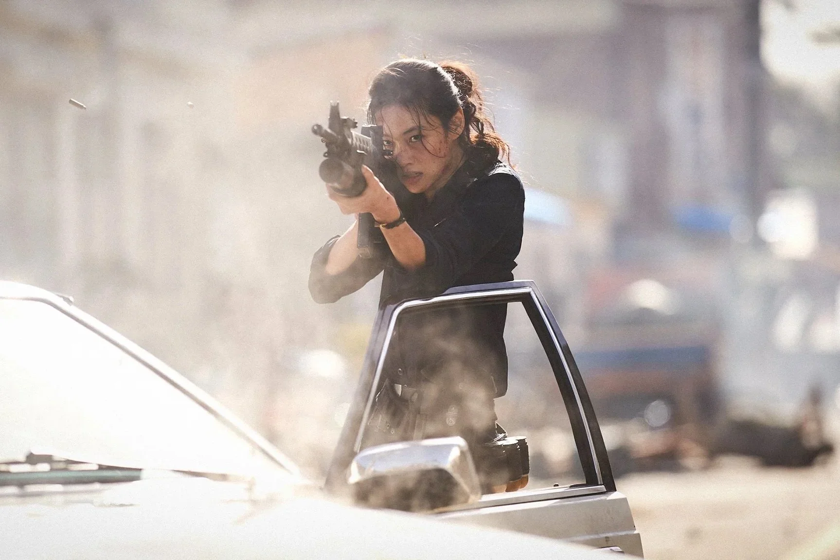 Sung-ae aims a gun from behind an open car door.