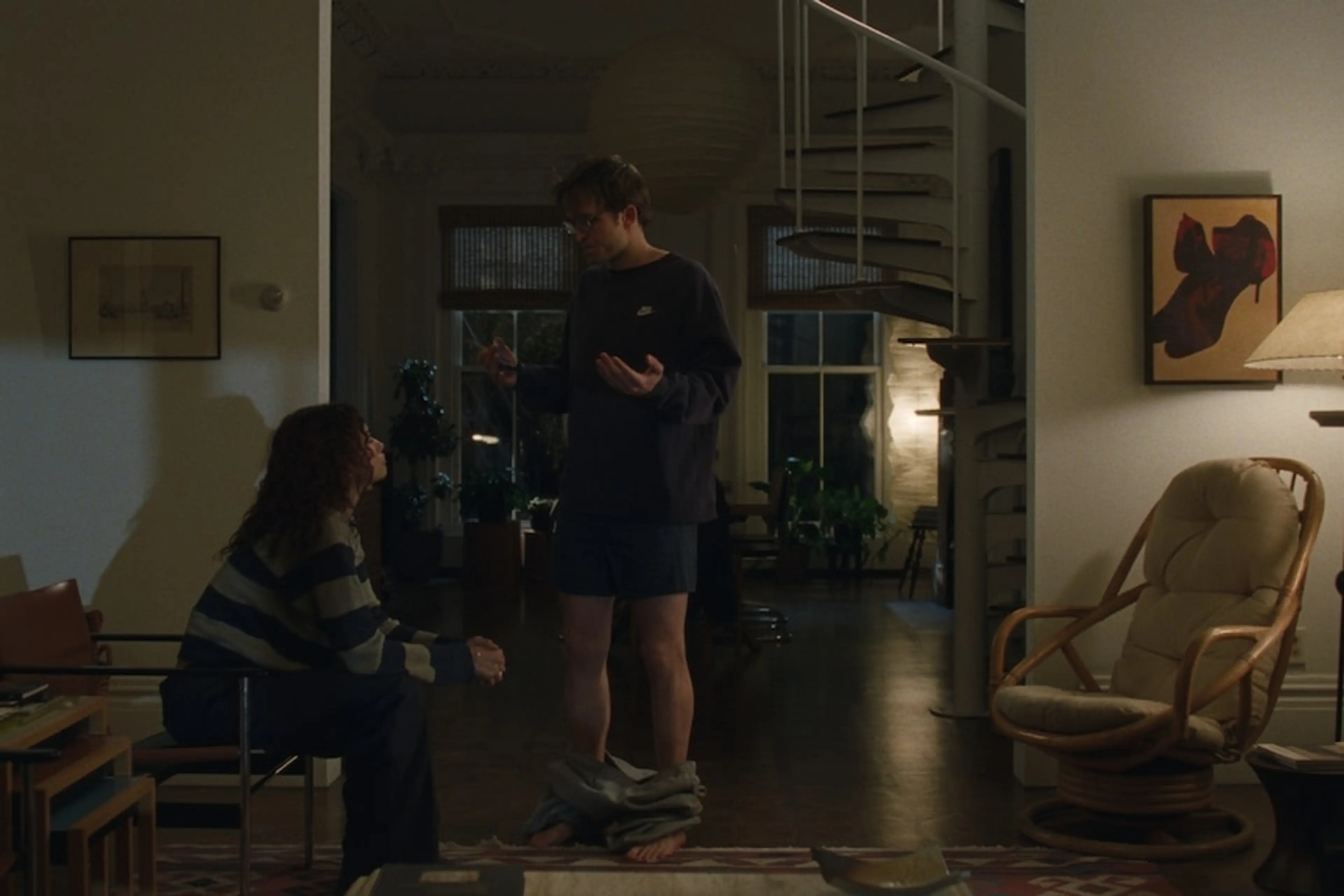 Emma sits facing Charlie, who gestures with his trousers around his ankles in their living room.