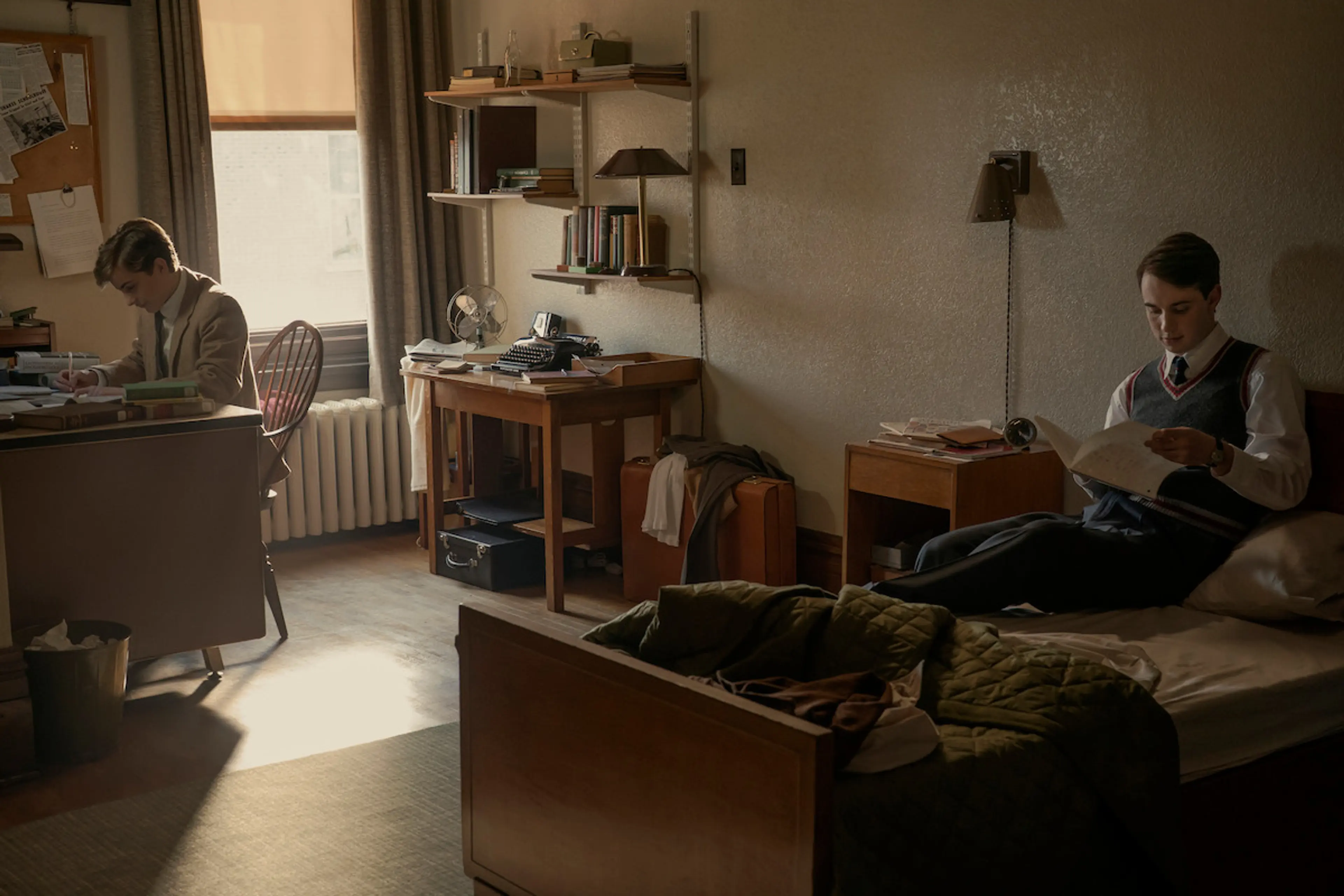 Two Harvard students read and write in a dorm room with books and papers on their desks.