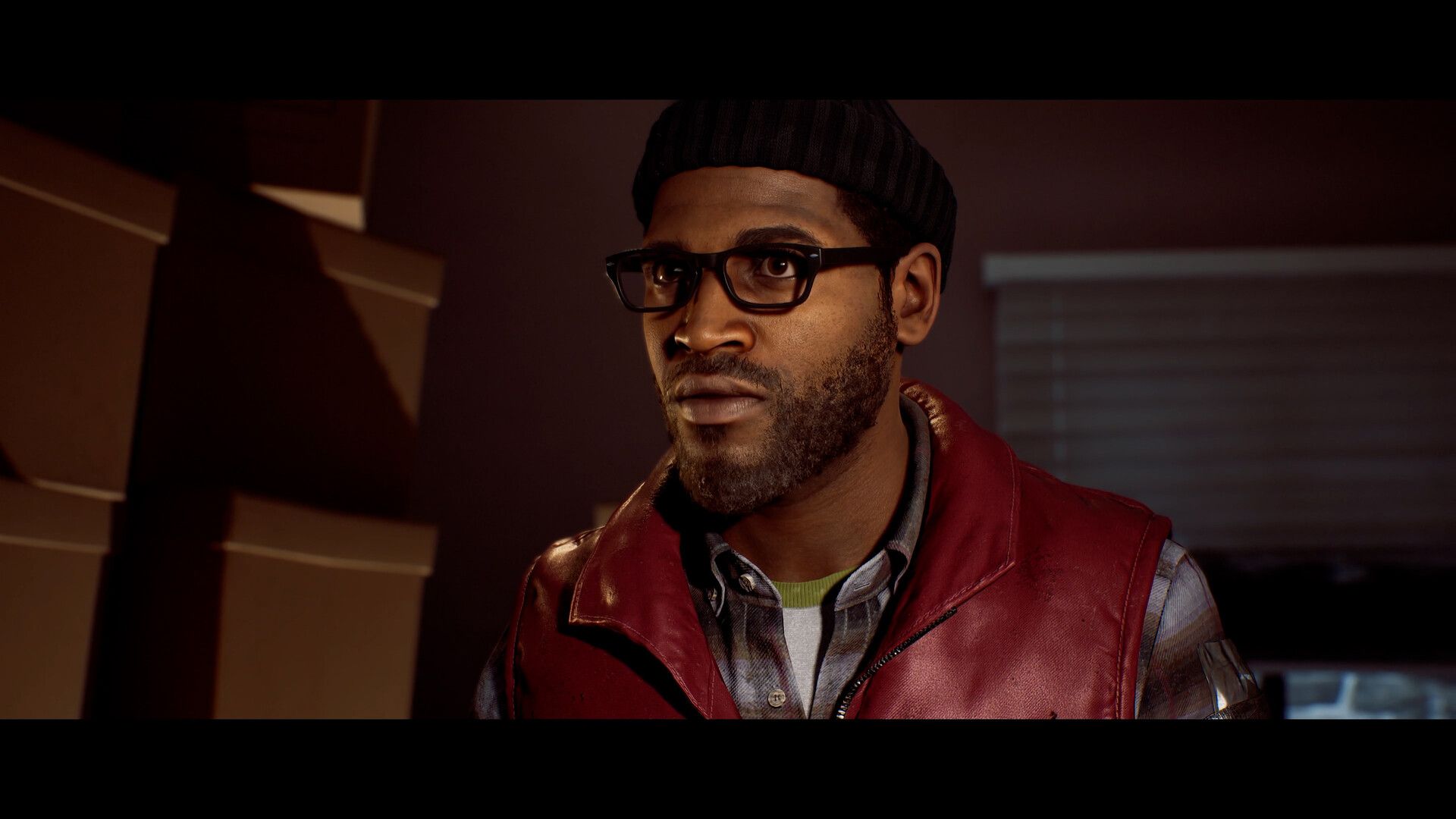 Simon Ordell looks towards someone in an indoor room while wearing glasses and a hat.
