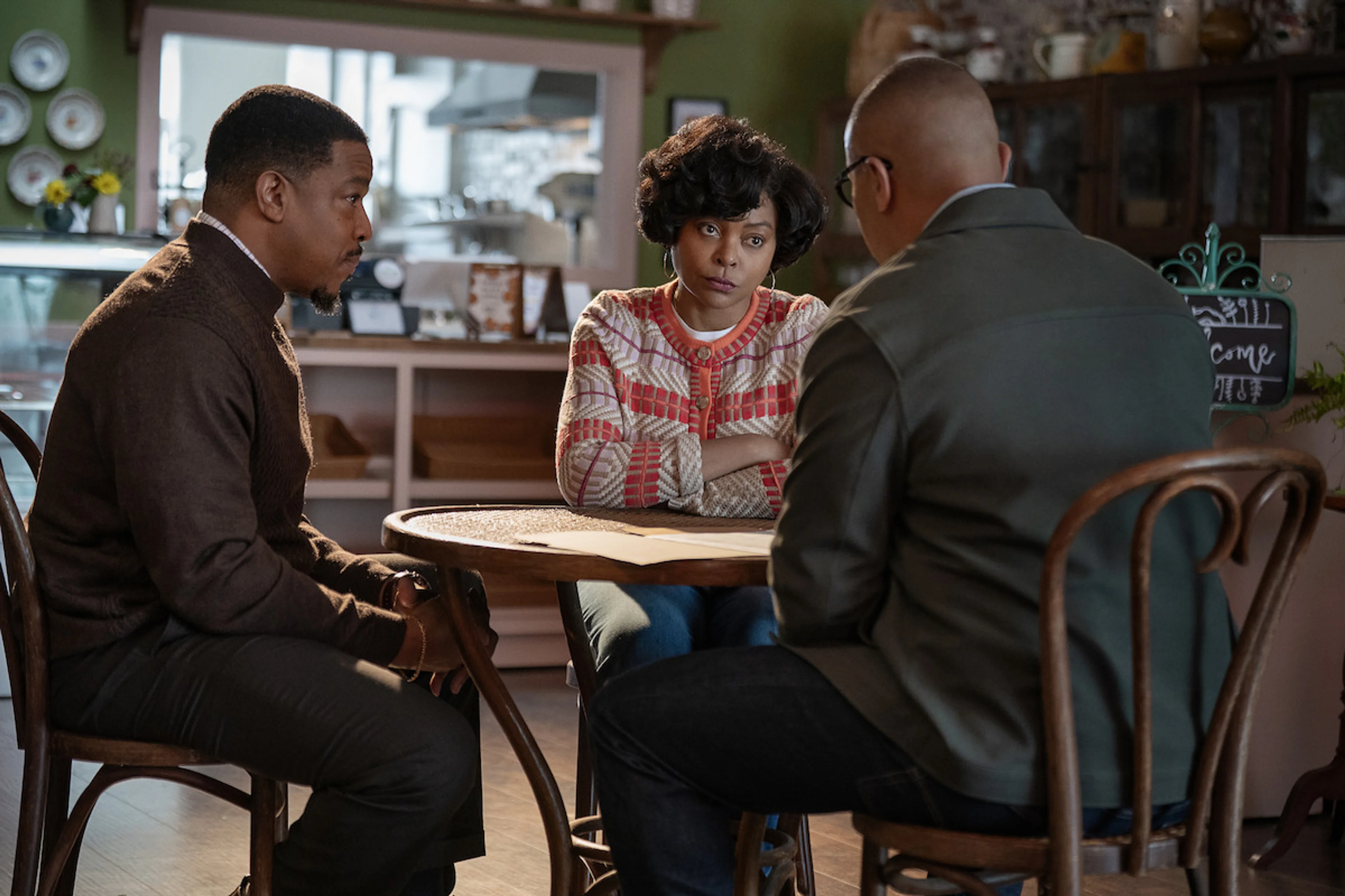 Three people talk around a table at a cafe in Give Me Some Sugah.