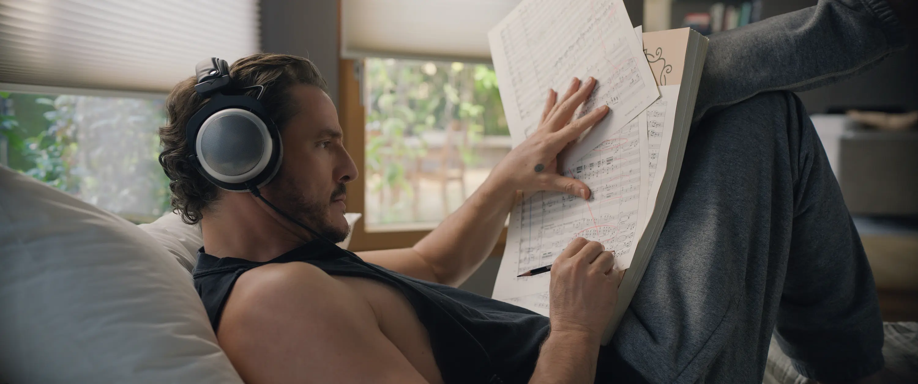 Pedro Pascal as Alex Serian studies sheet music while wearing headphones in Behemoth!.