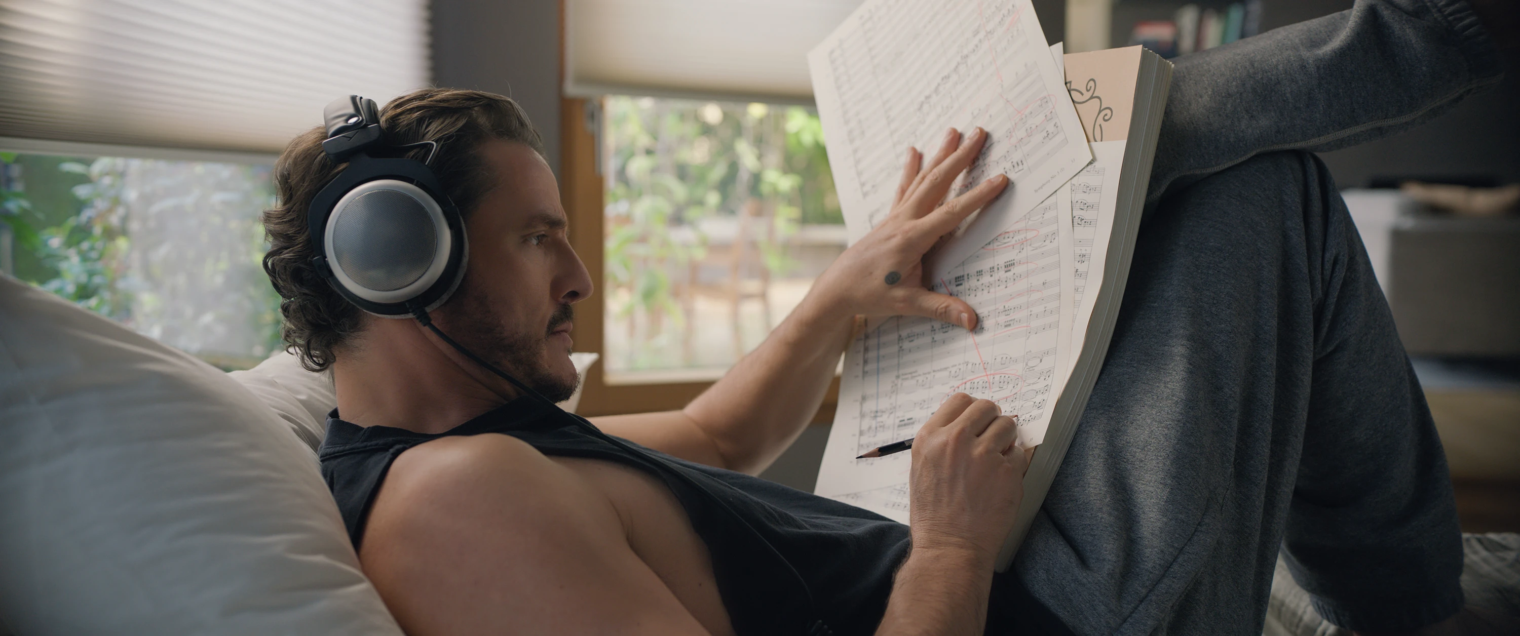 Pedro Pascal as Alex Serian studies sheet music while wearing headphones in Behemoth!.