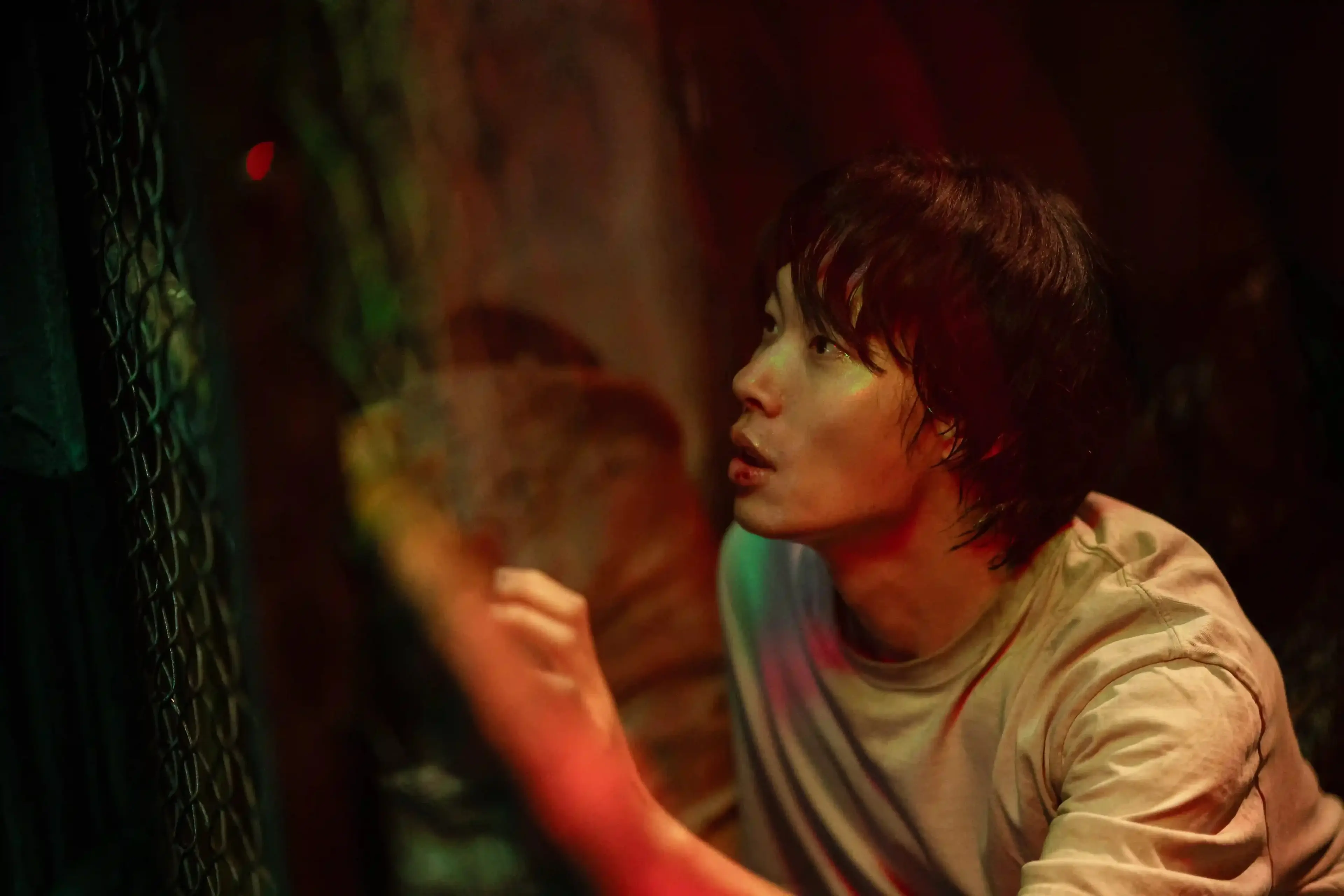 Ryu Jun-yeol’s character looks upward beside a tree under red and green light.