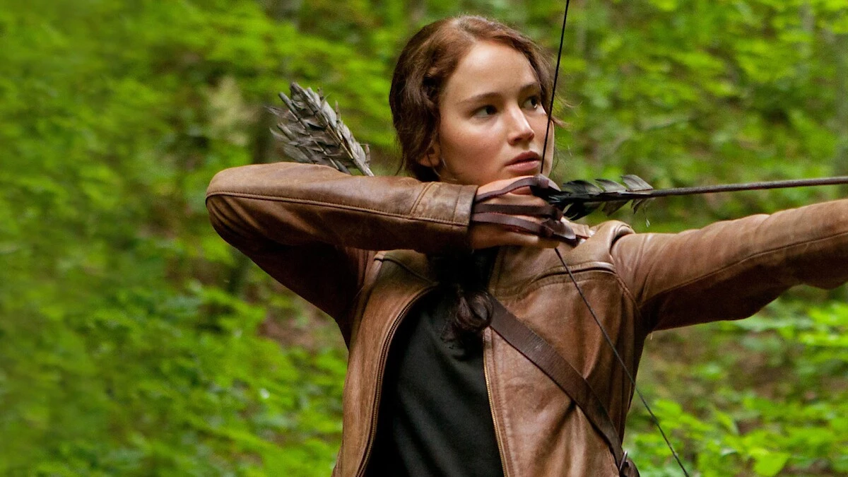 Katniss Everdeen aims her bow in a forest in The Hunger Games.