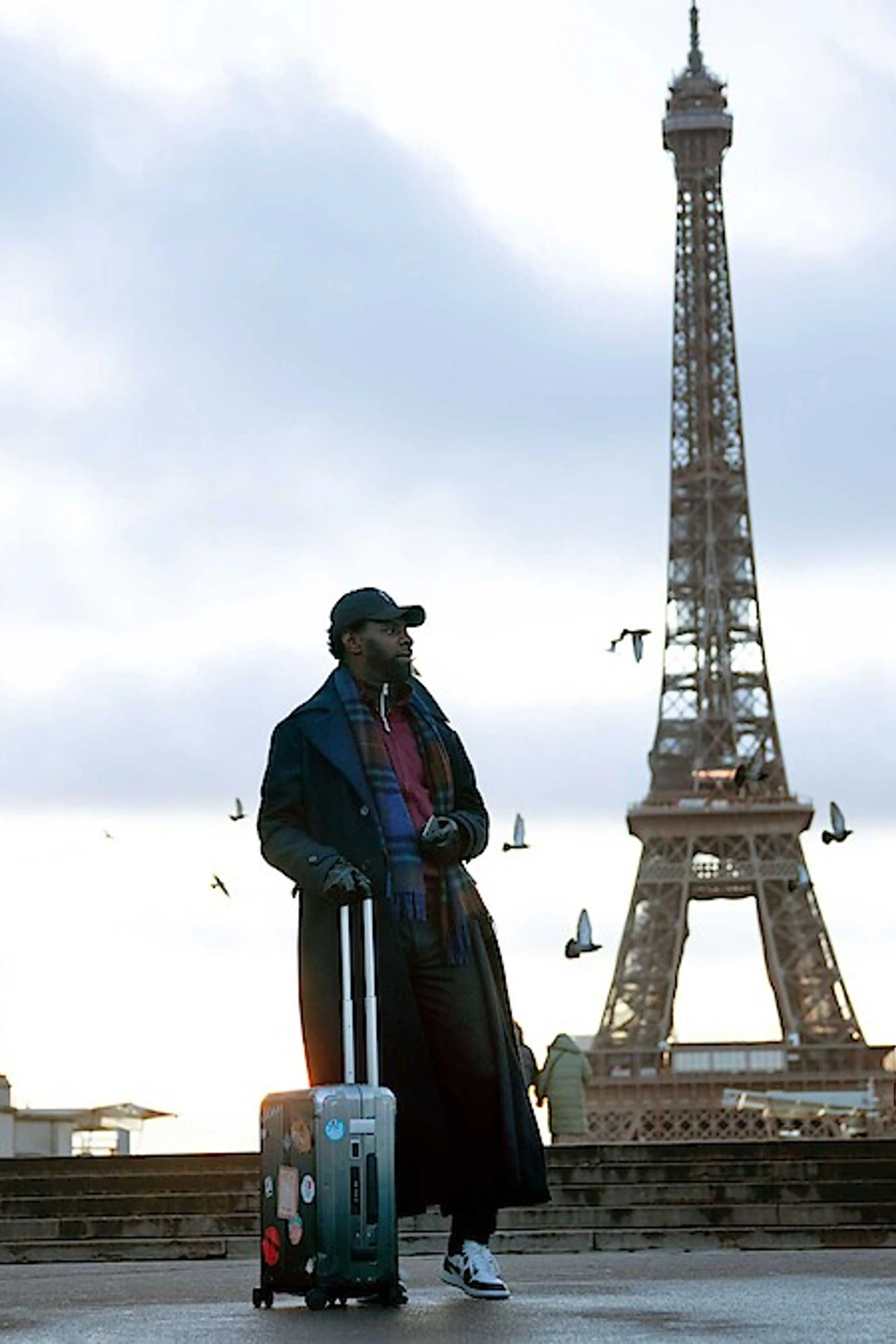 Omar Sy as Assane Diop stands with a suitcase in front of the Eiffel Tower in Lupin.