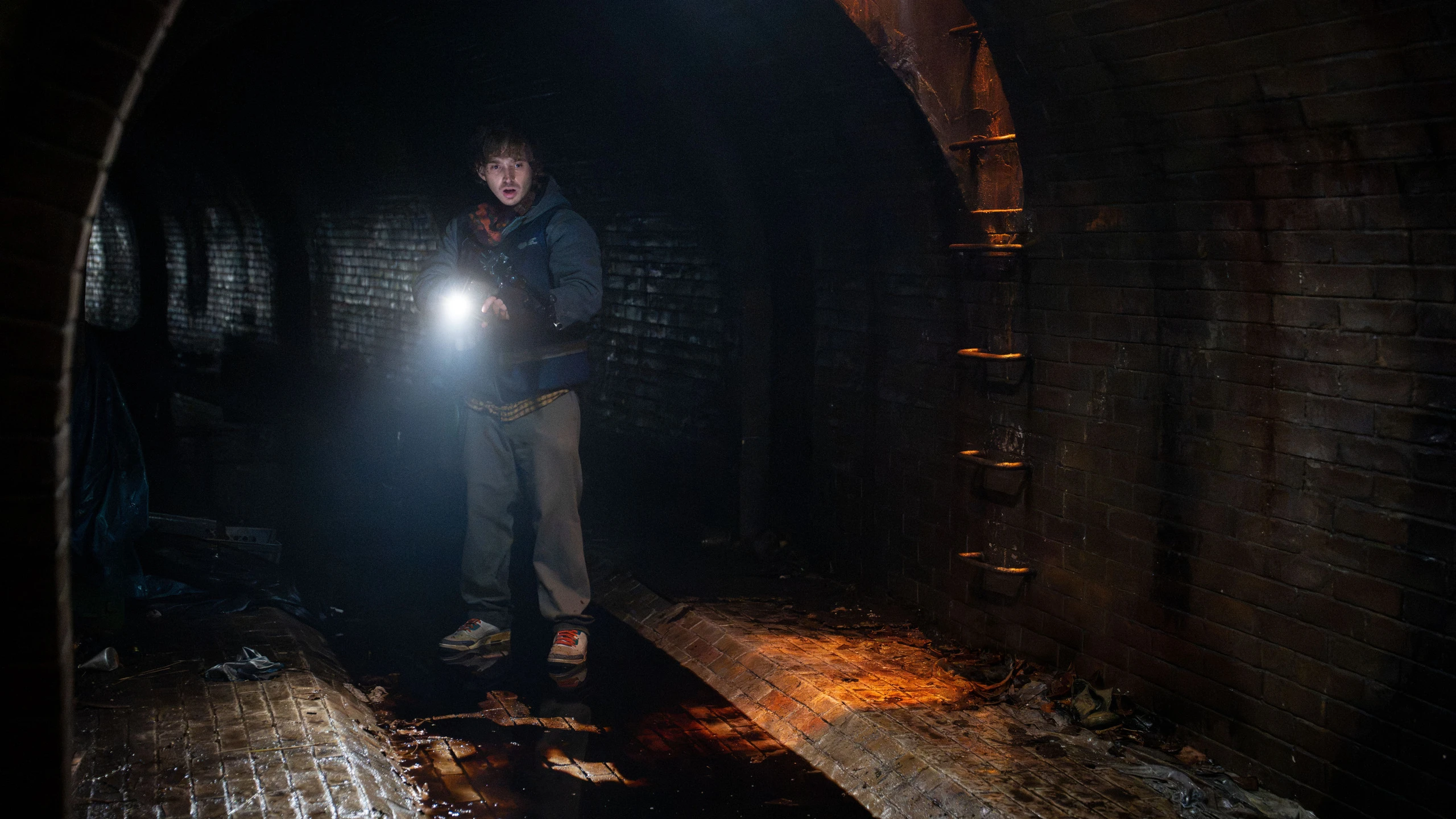 Bryan holds a flashlight beneath a brick arch in a dark tunnel.