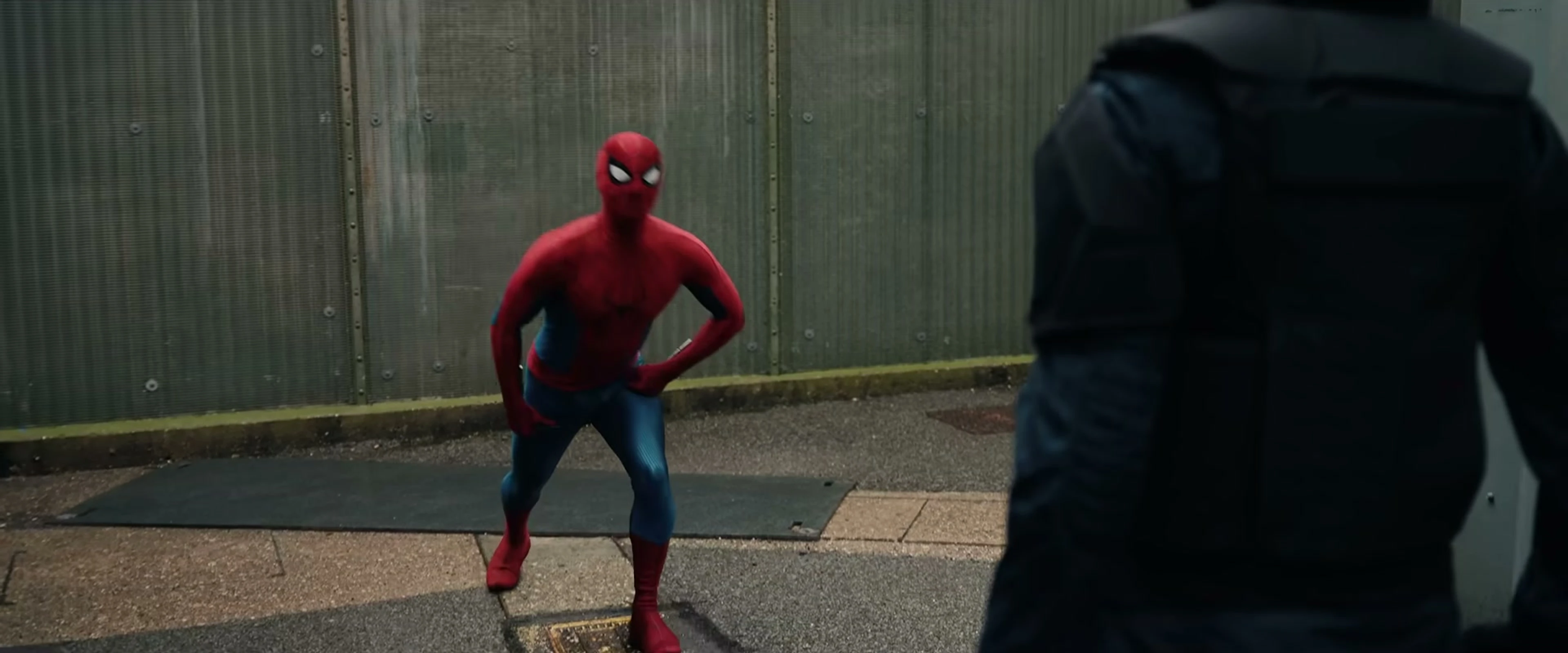 Spider-Man stands facing an armoured man in an outdoor service area.