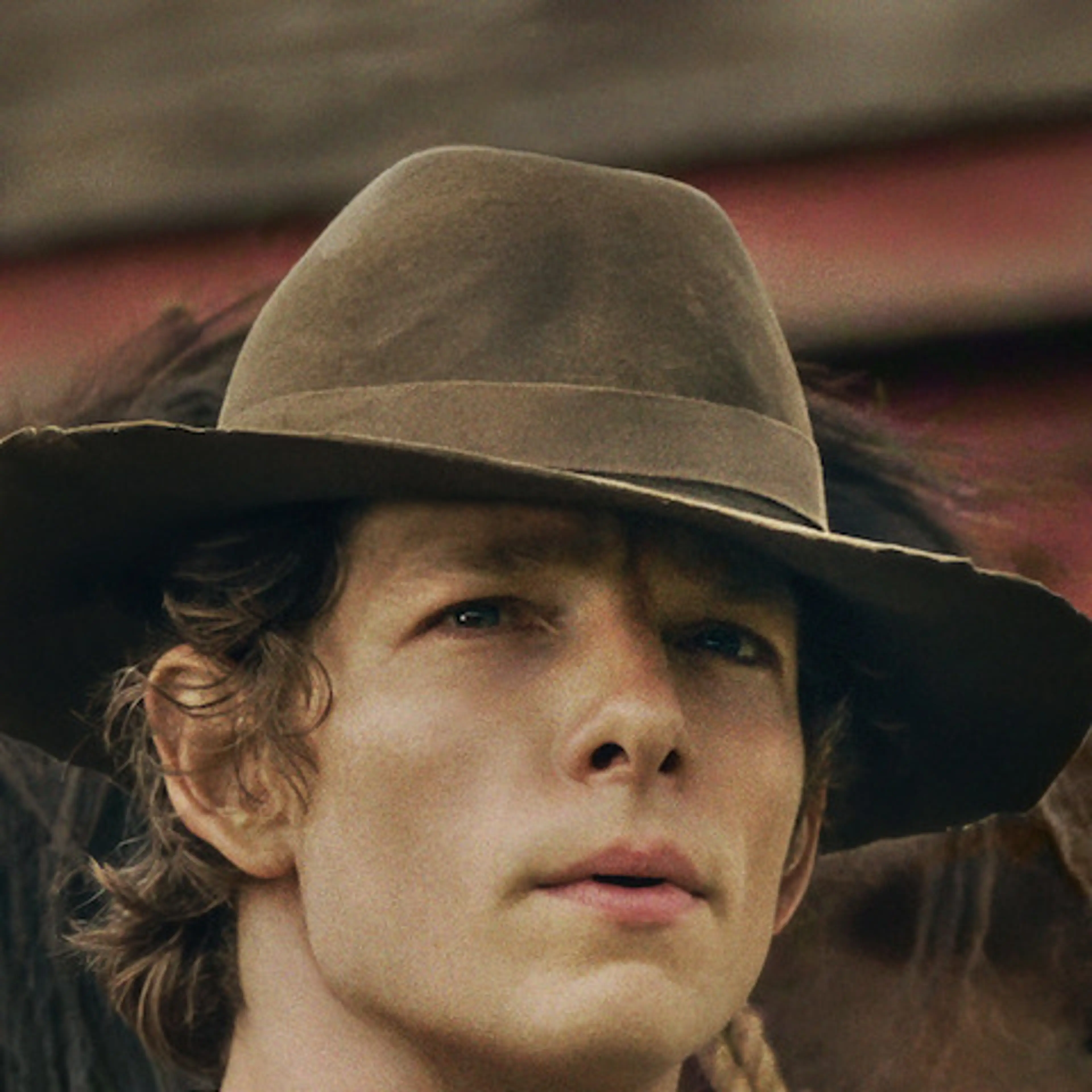 Mike Faist as Charles Trask, wearing a brown hat, beside a horse in East of Eden.