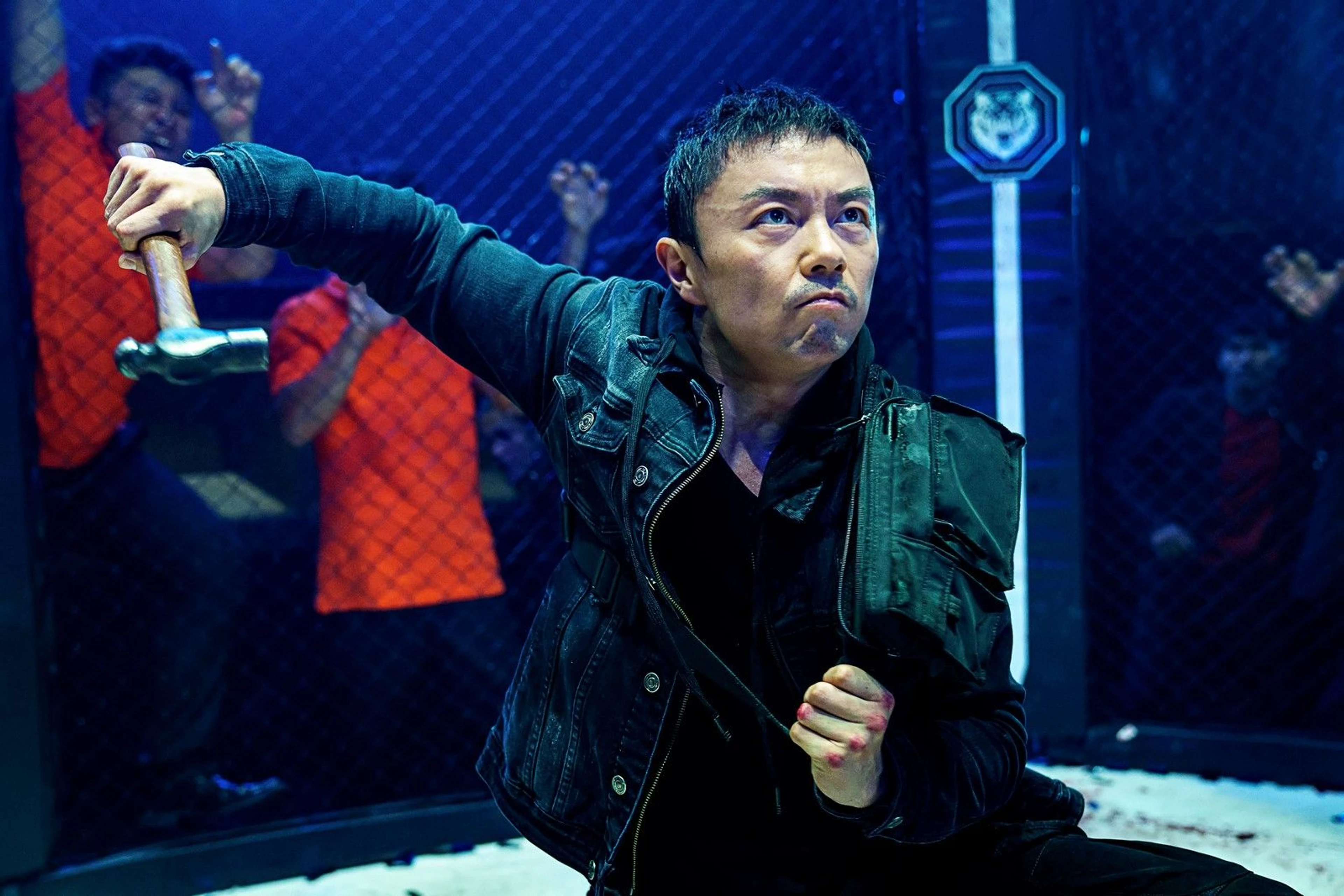 Xie Miao as Wang Wei raises a hammer inside a fighting cage.