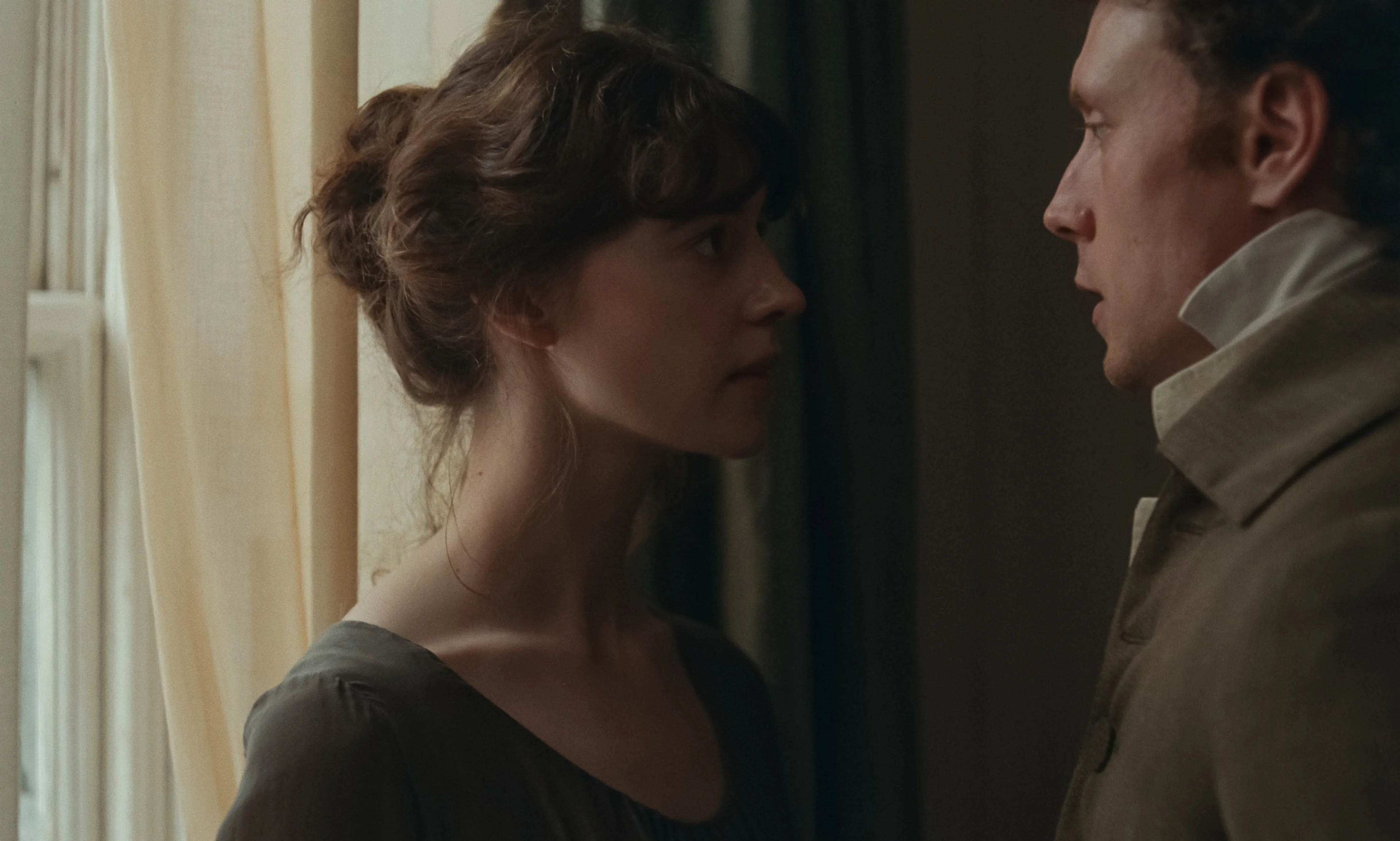Elinor and Edward stand close together beside a window.