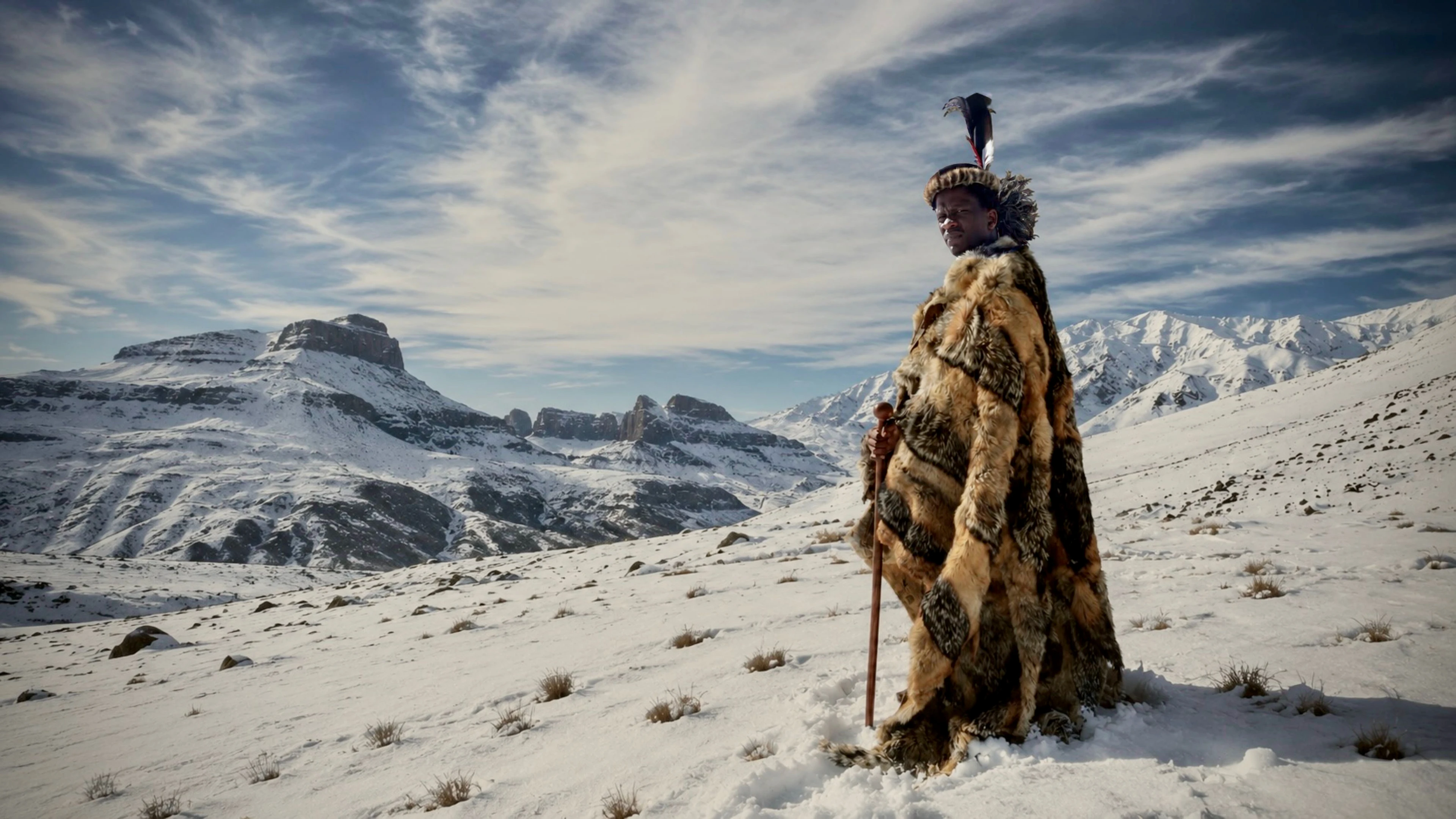 Lemogang Tsipa as King Shaka, wearing a fur cloak on a snowy mountain.