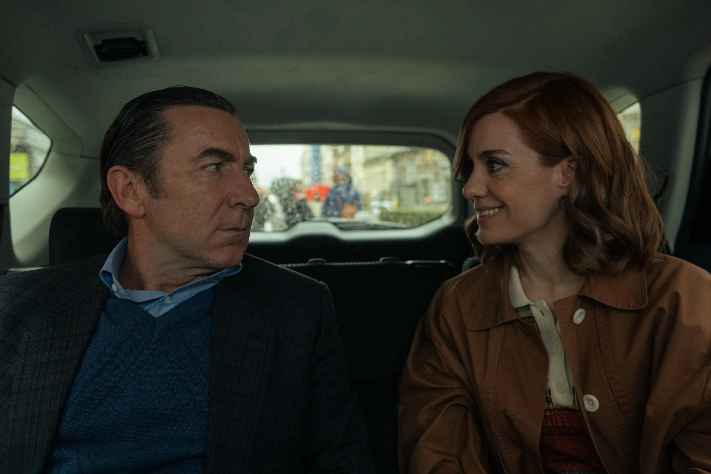 Don Leandro and Sofía sit together in the back seat of a car.