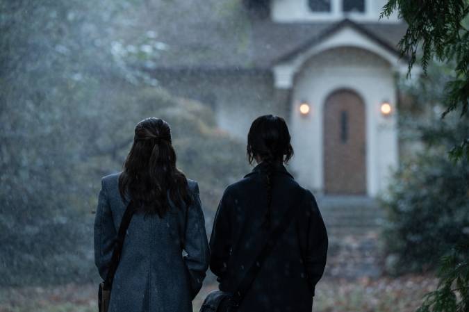 The two missionaries stand in the rain facing the front door of a house.