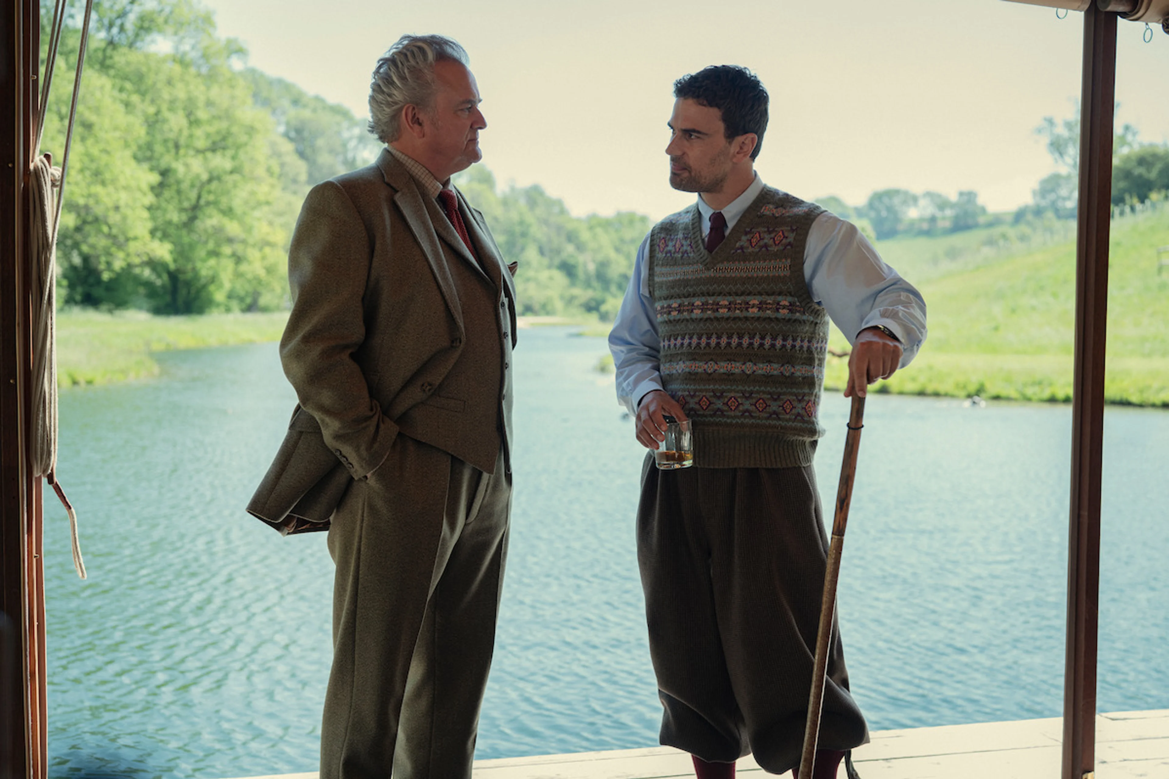Hugh Bonneville as Lord Hawthorne and Theo James as Eddie Horniman speak beside a lake during the country gathering.