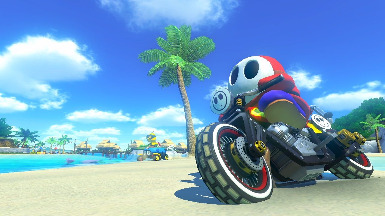 Shy Guy rides a motorbike beside a bright blue sea and beach.