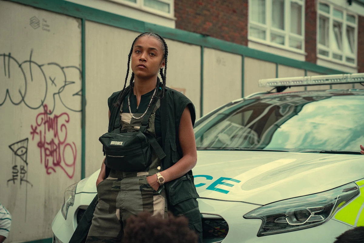 Jasmine Jobson as Jaq stands beside a police car in Top Boy.