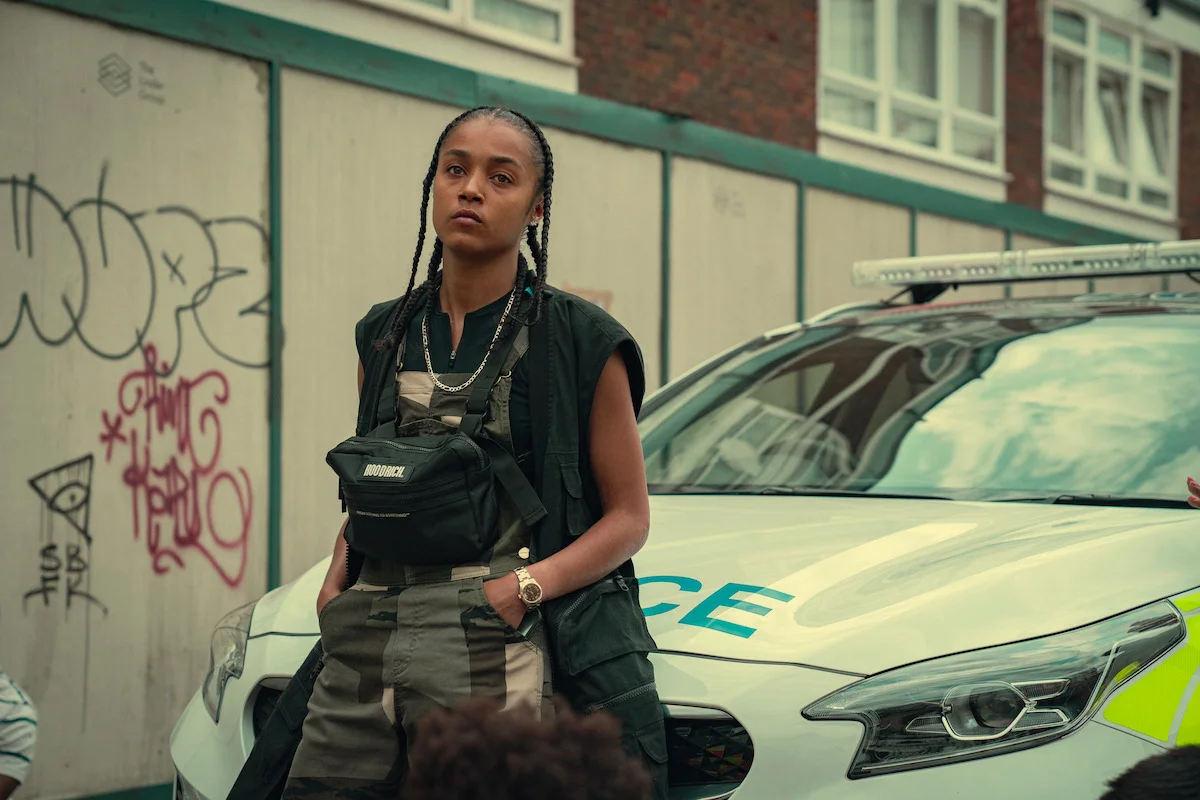 Jasmine Jobson as Jaq stands beside a police car in Top Boy.