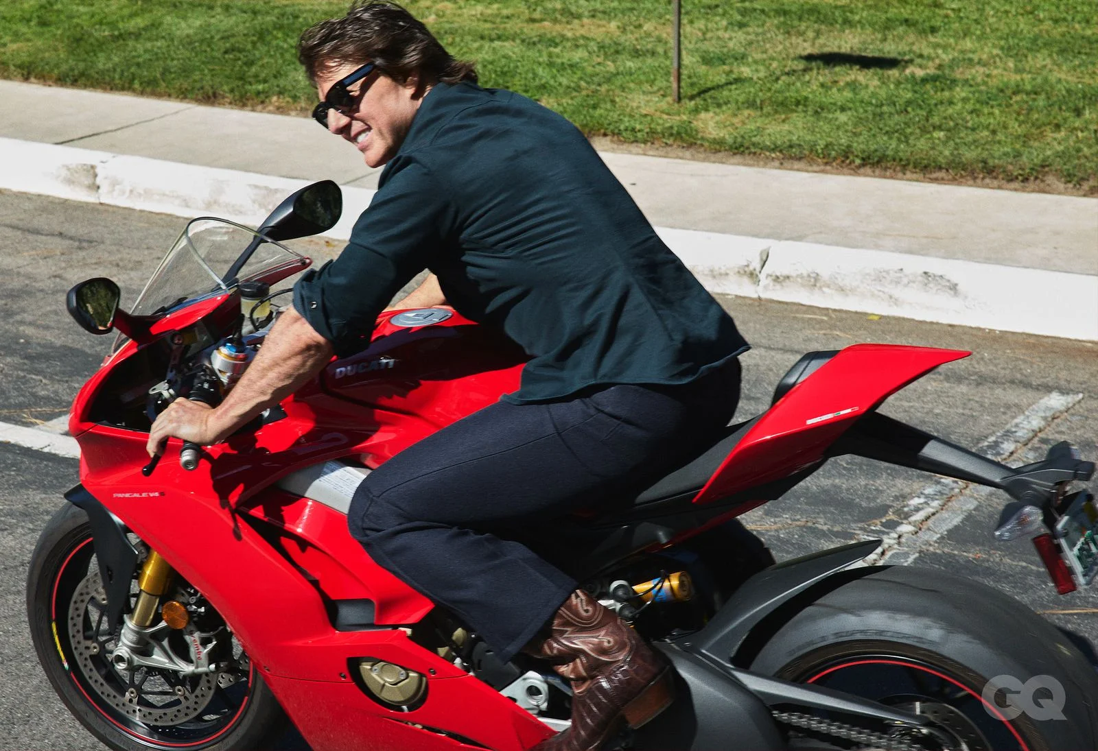 Tom Cruise smiling on a red motorcycle in a dark shirt and sunglasses.