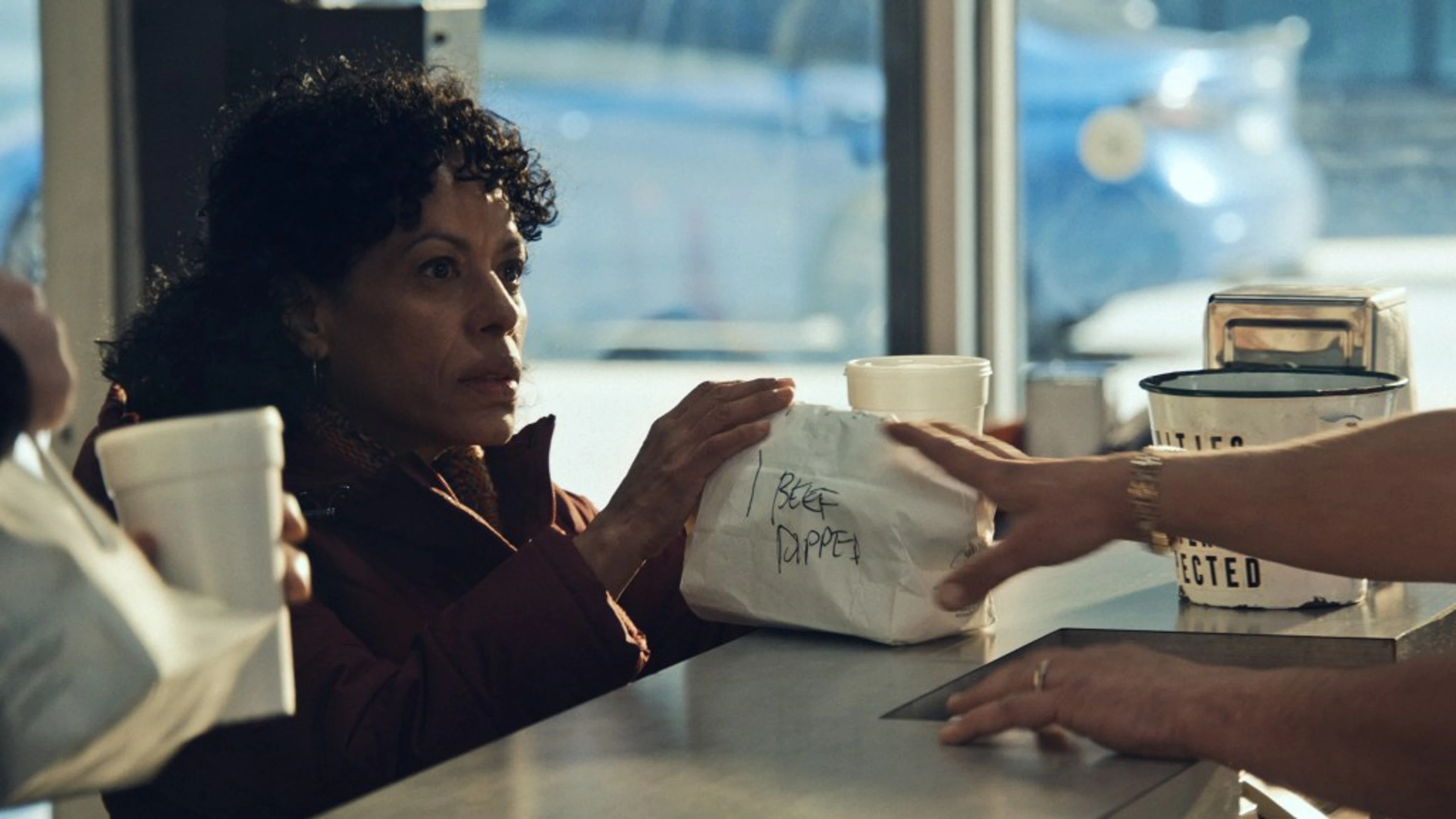 Tina, played by Liza Colón-Zayas, receives a paper-wrapped sandwich at the counter in “Napkins”.