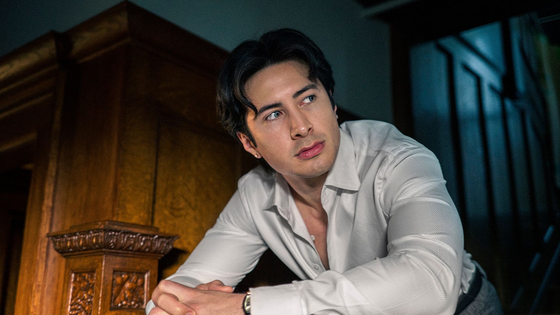 Hudson Williams as Henry Park wears an open white shirt.