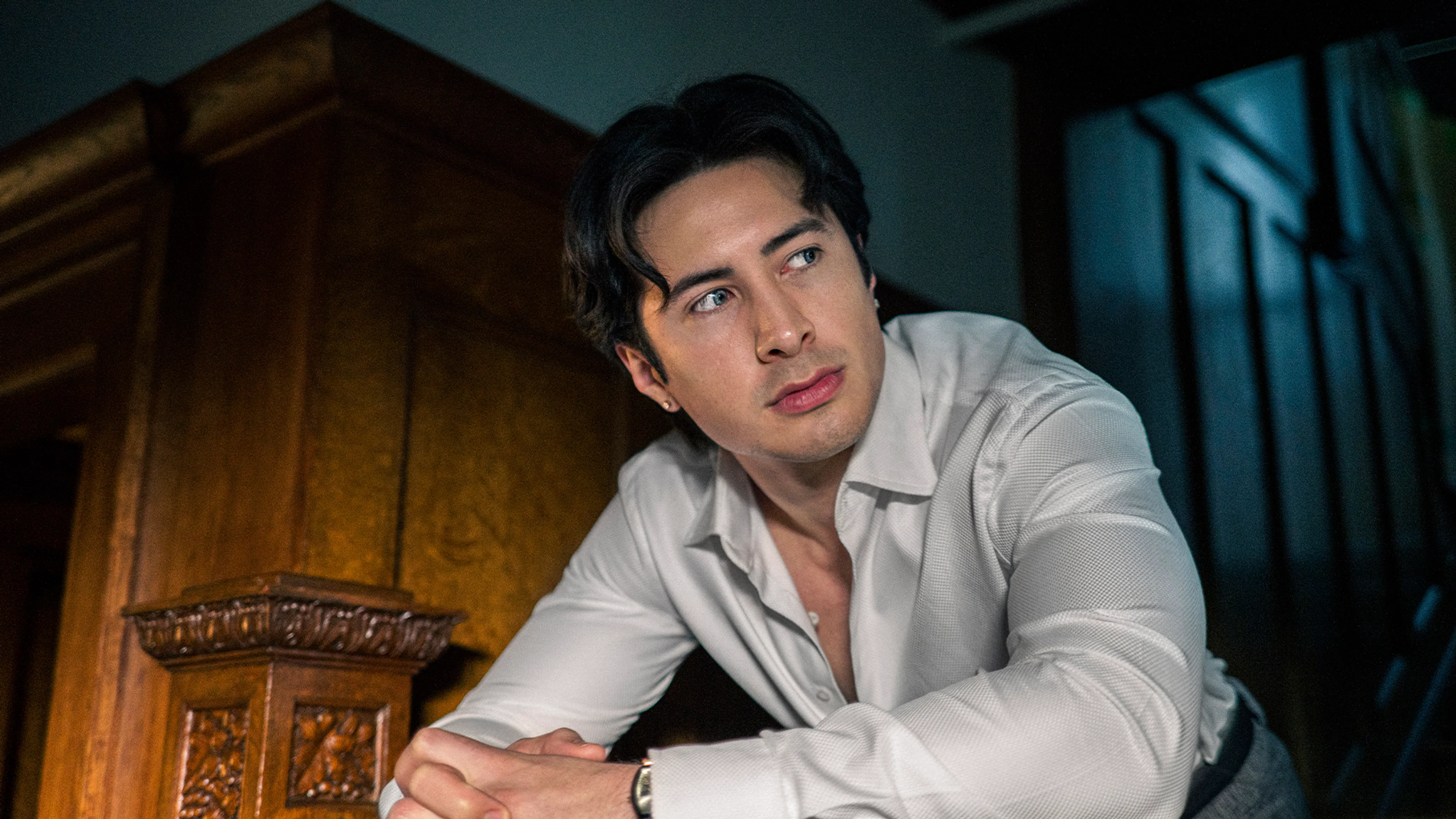 Hudson Williams as Henry Park wears an open white shirt.