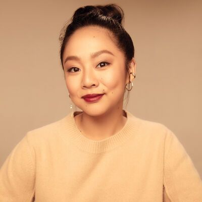 Stephanie Hsu wears a cream sweater with her hair in a bun against a tan background.