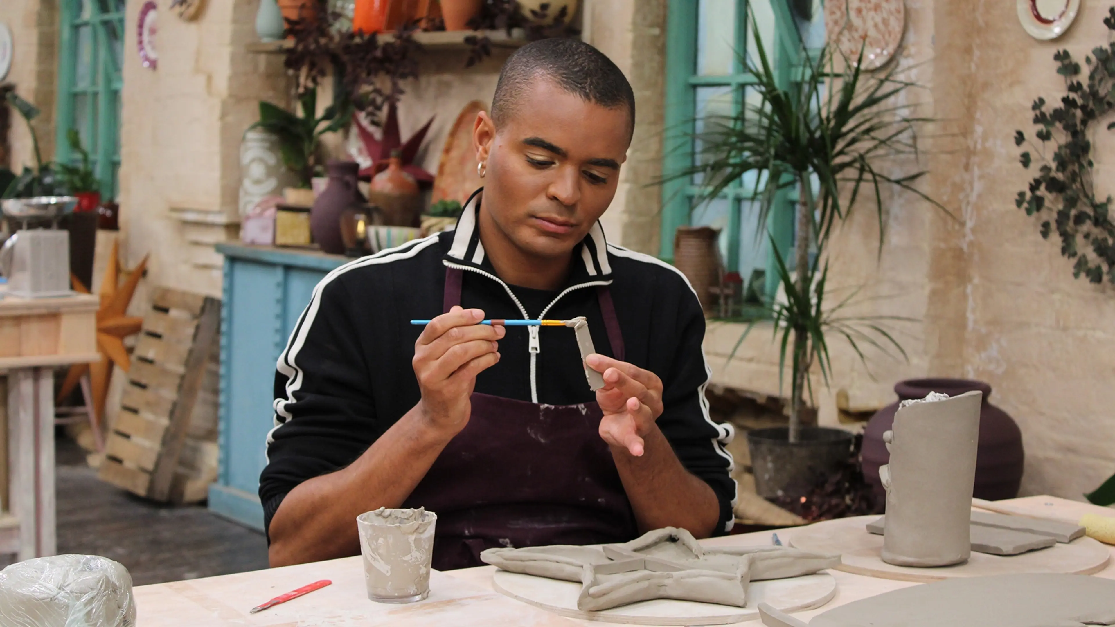 Layton Williams paints a small clay piece beside a desk-set sculpture in the pottery.
