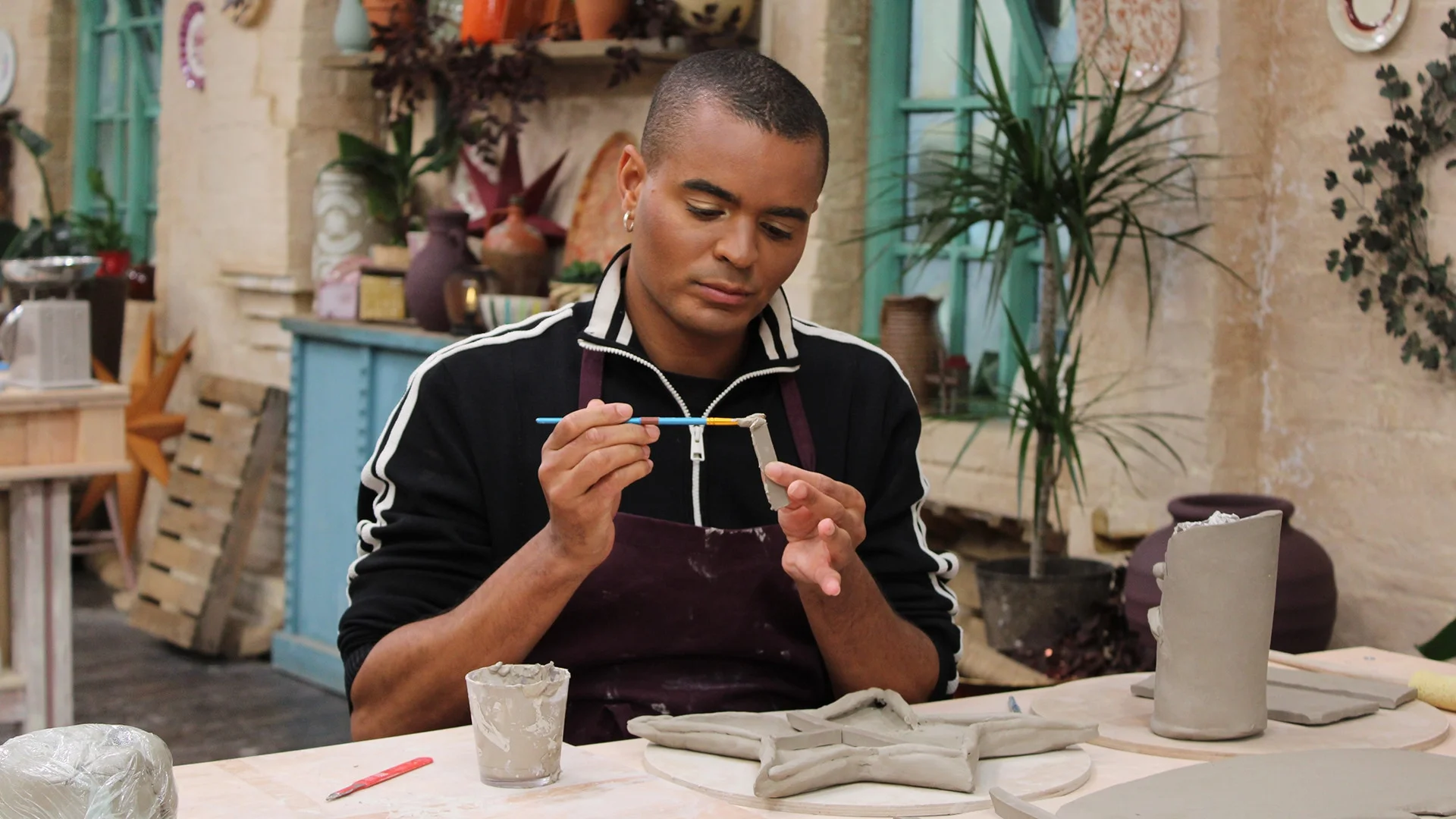 Layton Williams paints a small clay piece beside a desk-set sculpture in the pottery.