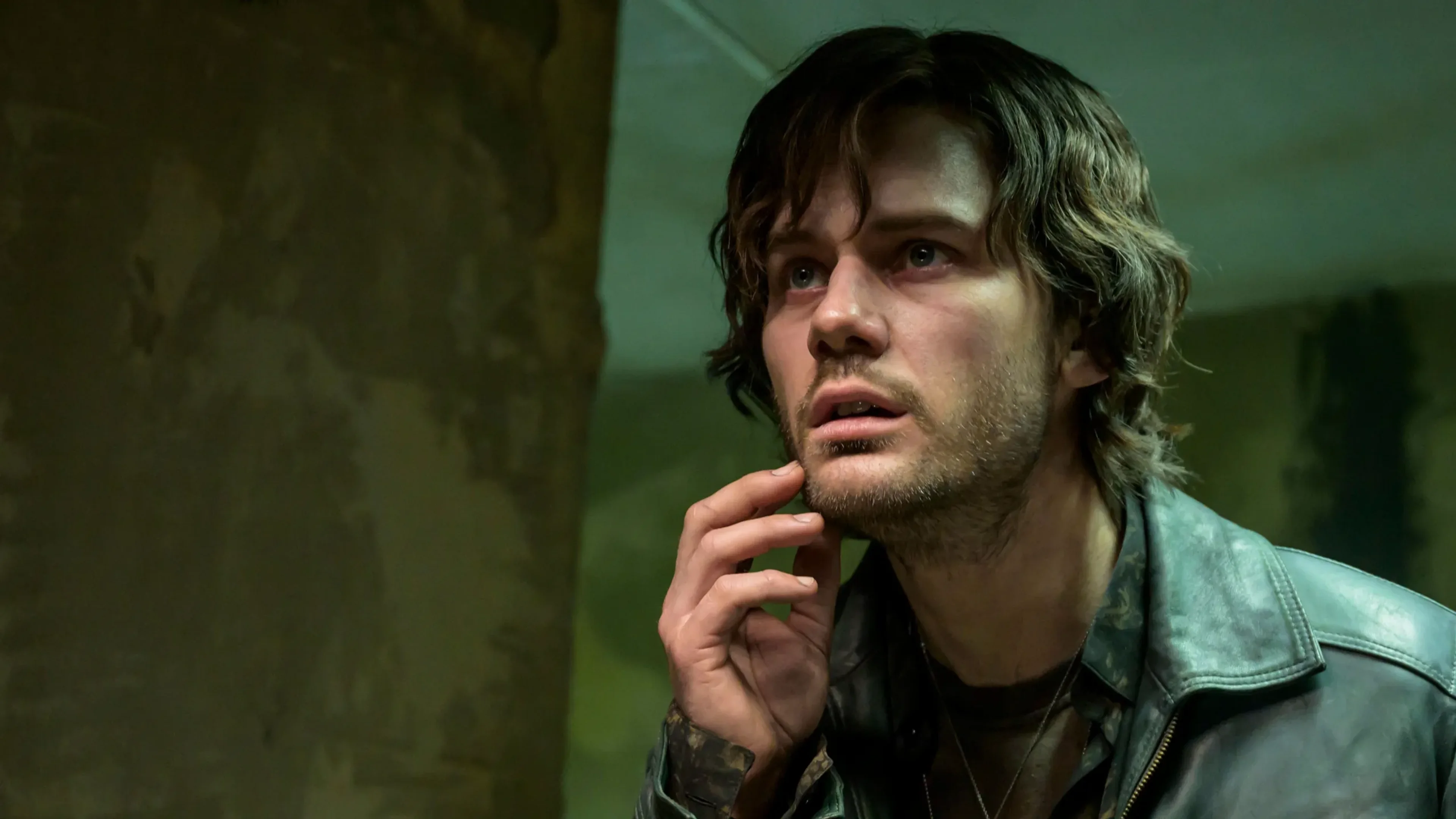 Jeremy Irvine as James looks frightened inside a dim green room in Return to Silent Hill.