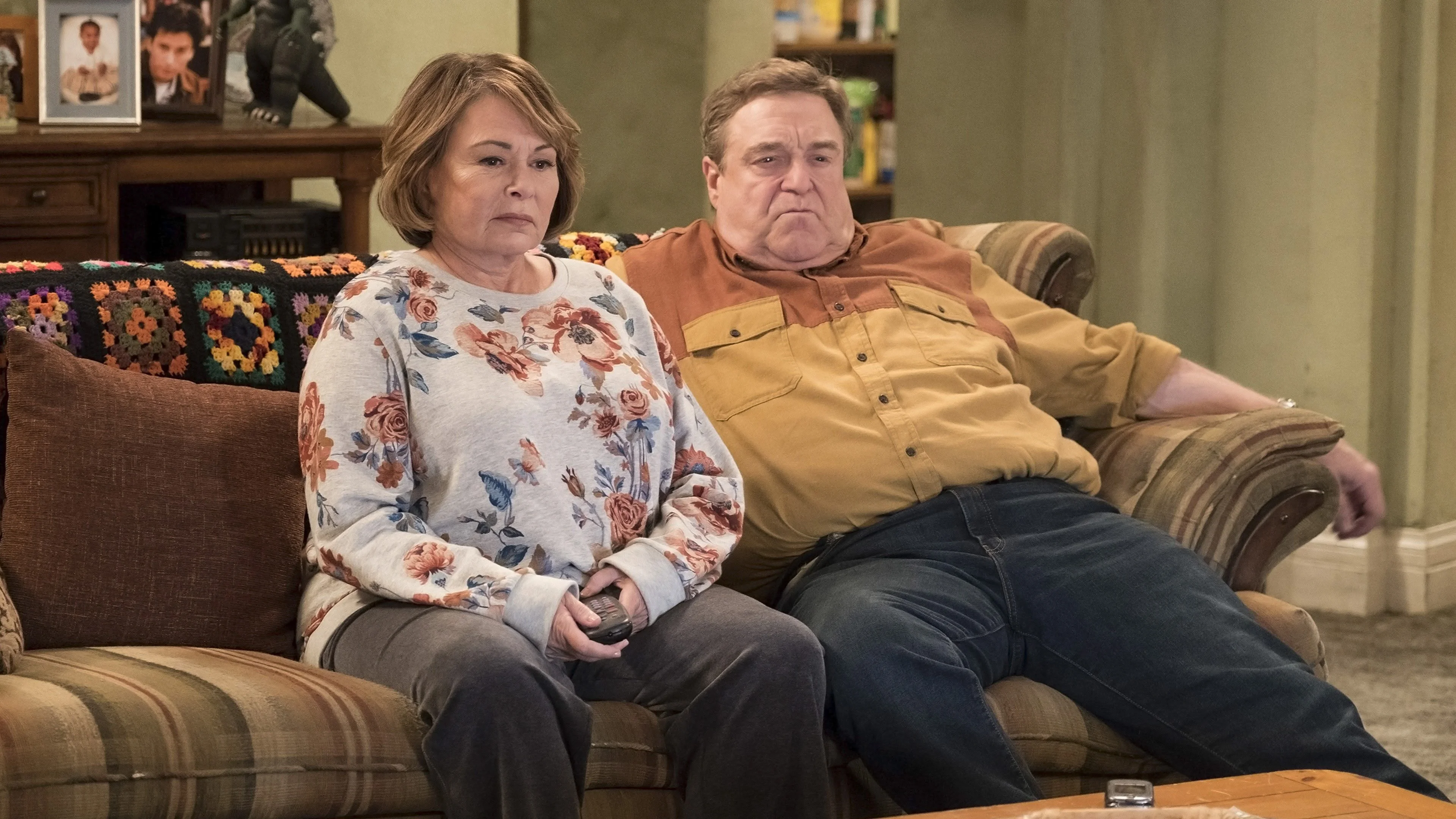 Roseanne Barr and John Goodman as Roseanne and Dan Conner sit on their living-room couch in season ten.