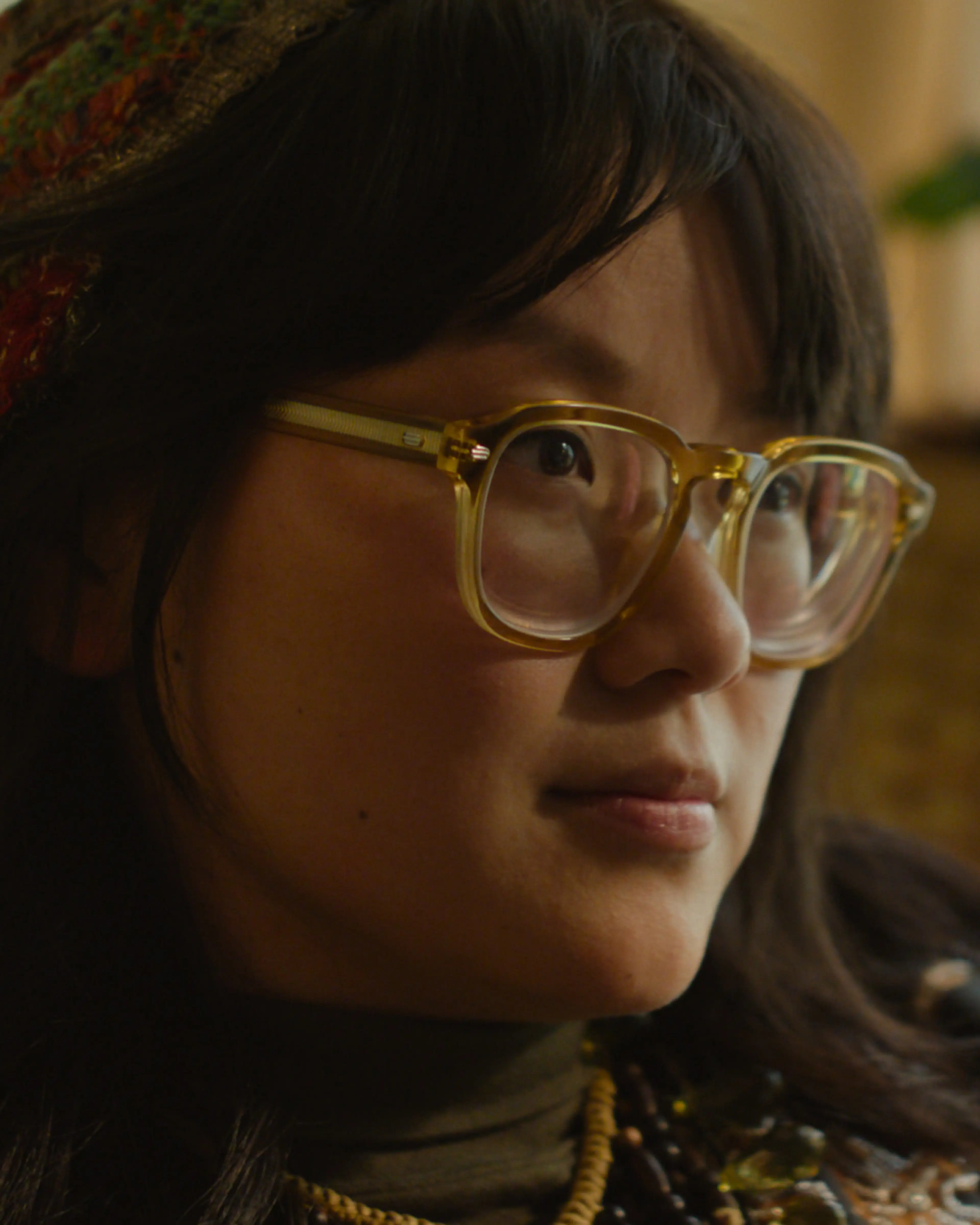 Thaddea Graham as Susie wears glasses and a red knitted hat.