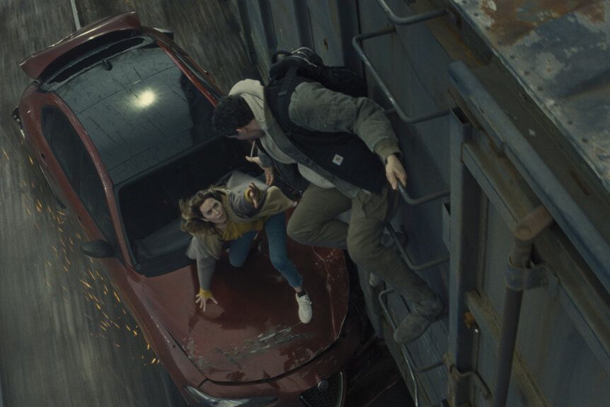 Daniel helps Margaret climb from a red car onto a moving train.