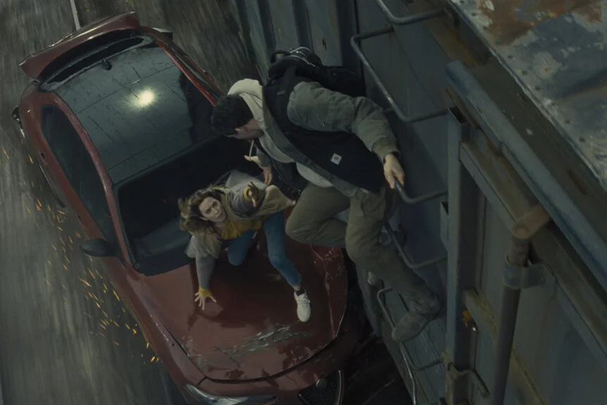 Daniel helps Margaret climb from a red car onto a moving train.
