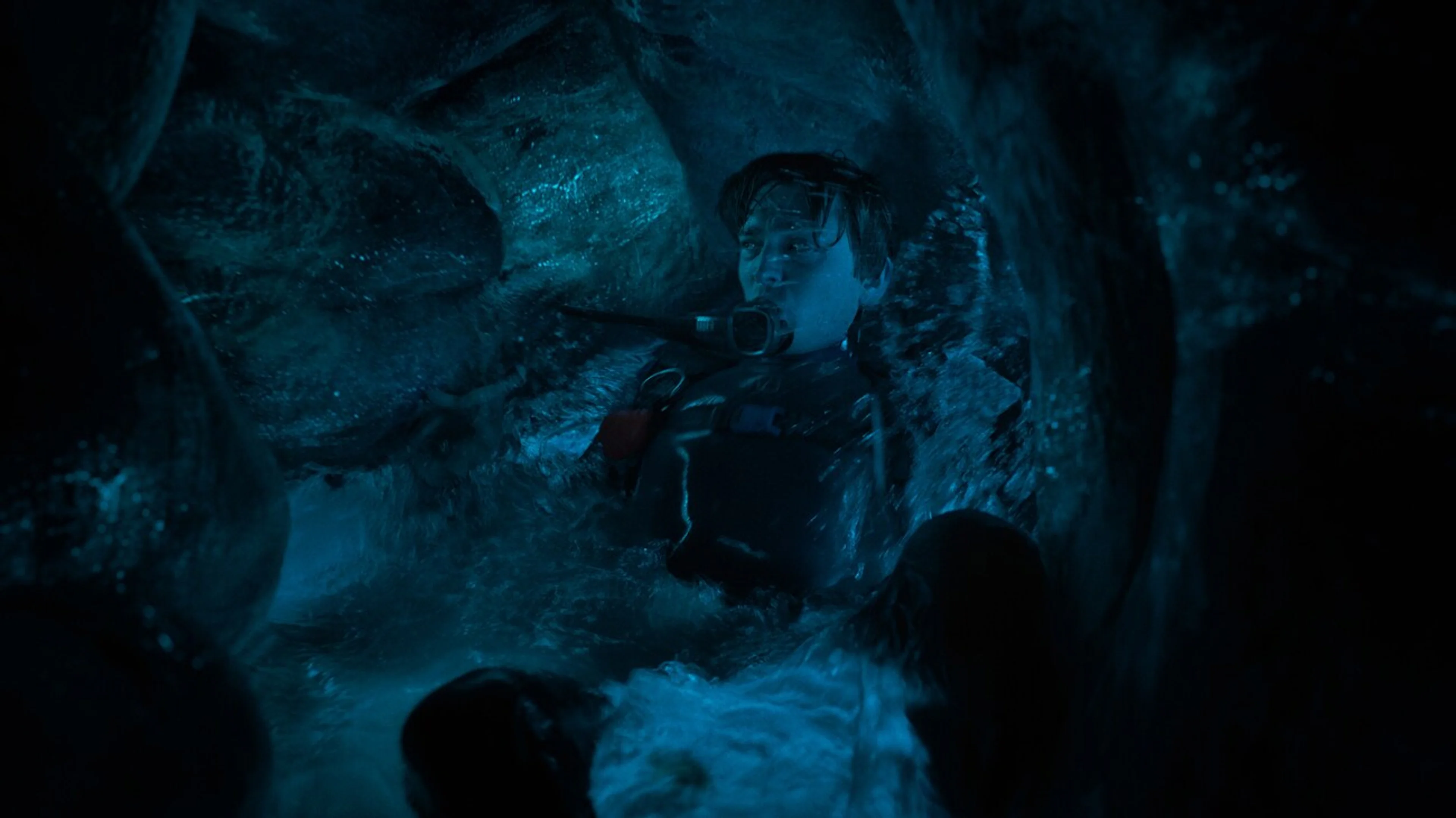 A scuba diver moves through a dark underwater space.