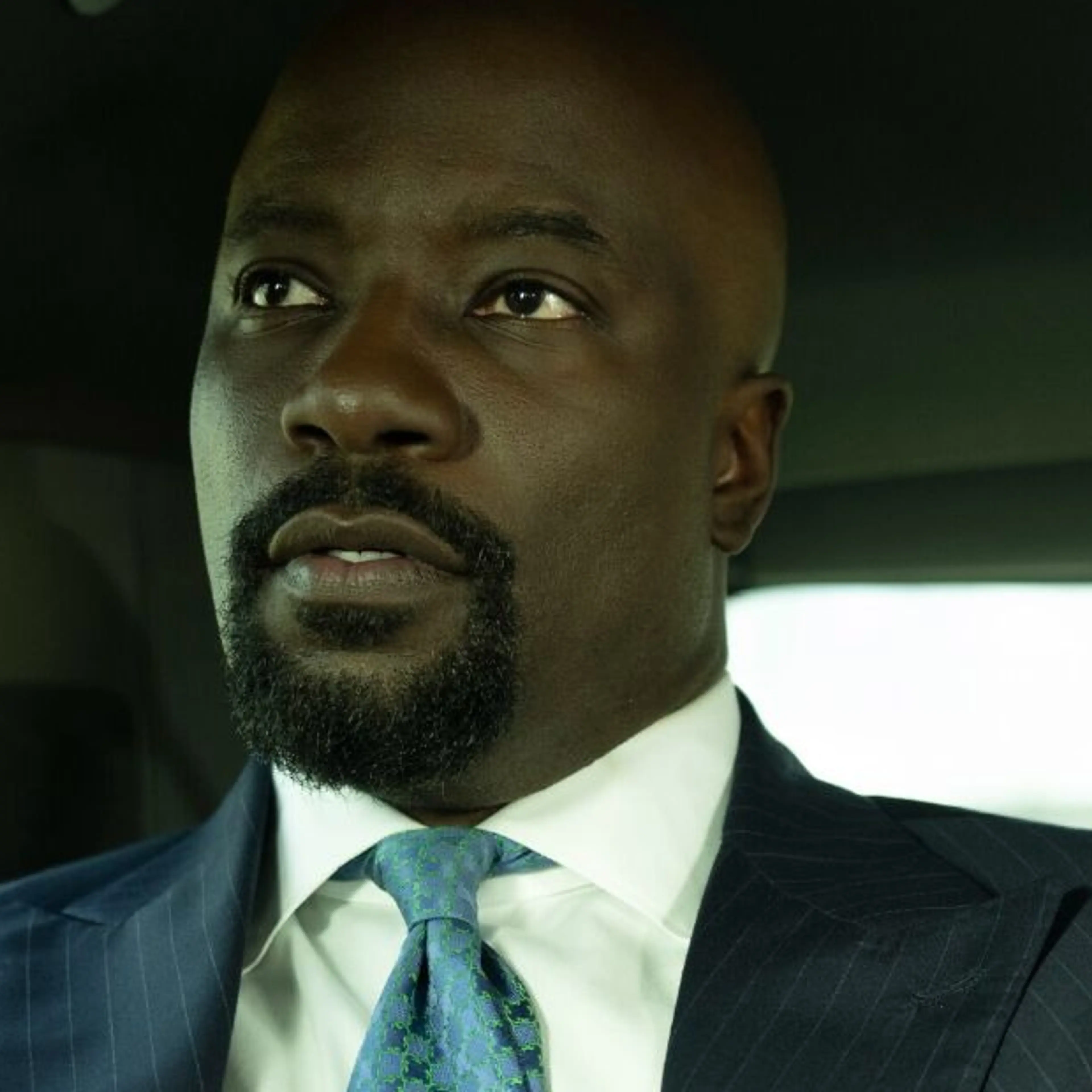 Mike Colter as Michael Price, wearing a dark suit and blue tie in an official Cupertino production photograph.