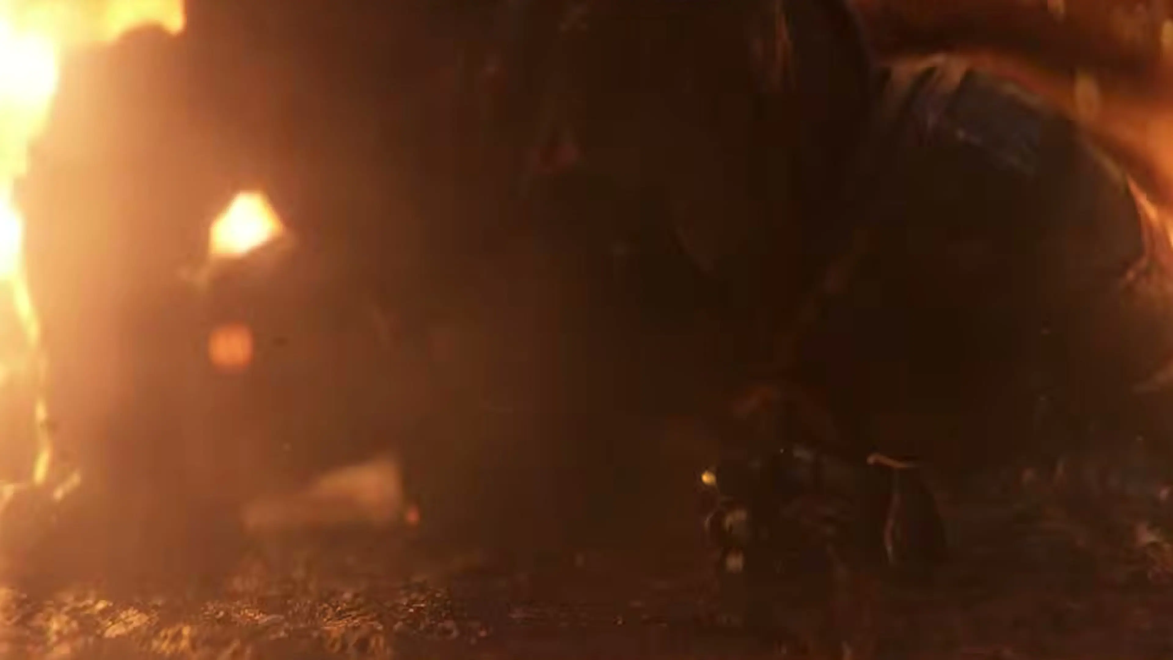 An armored figure kneels on the ground as flames burn behind them.