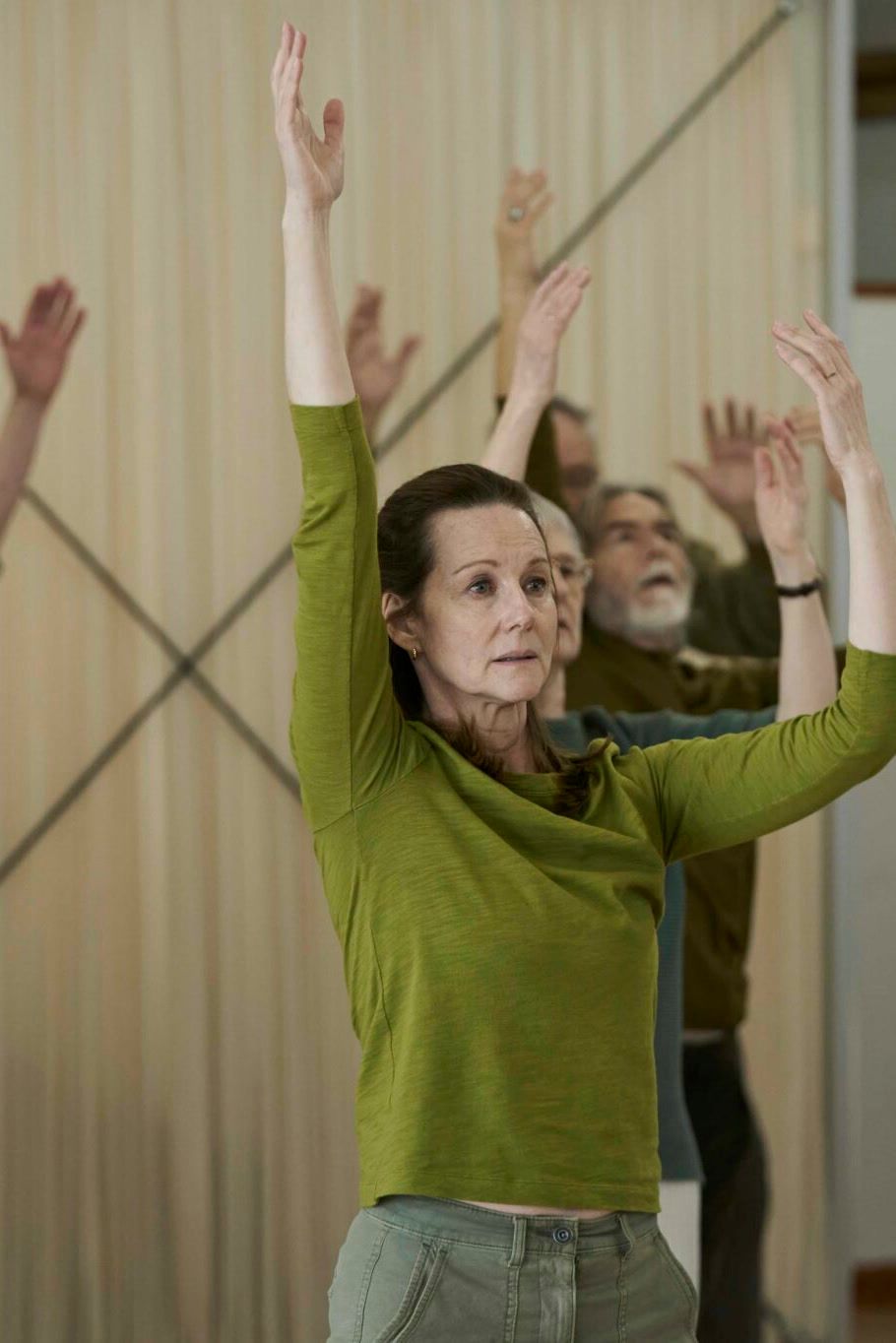 Laura Linney as Emma raises both arms during a movement class in Onwards and Sideways.