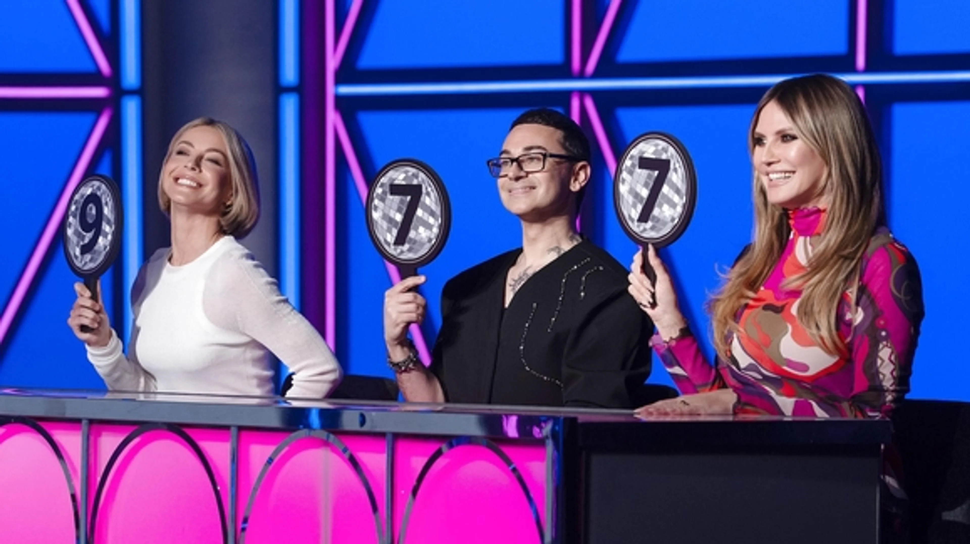 Project Runway judges hold score paddles on the Season 22 runway set.