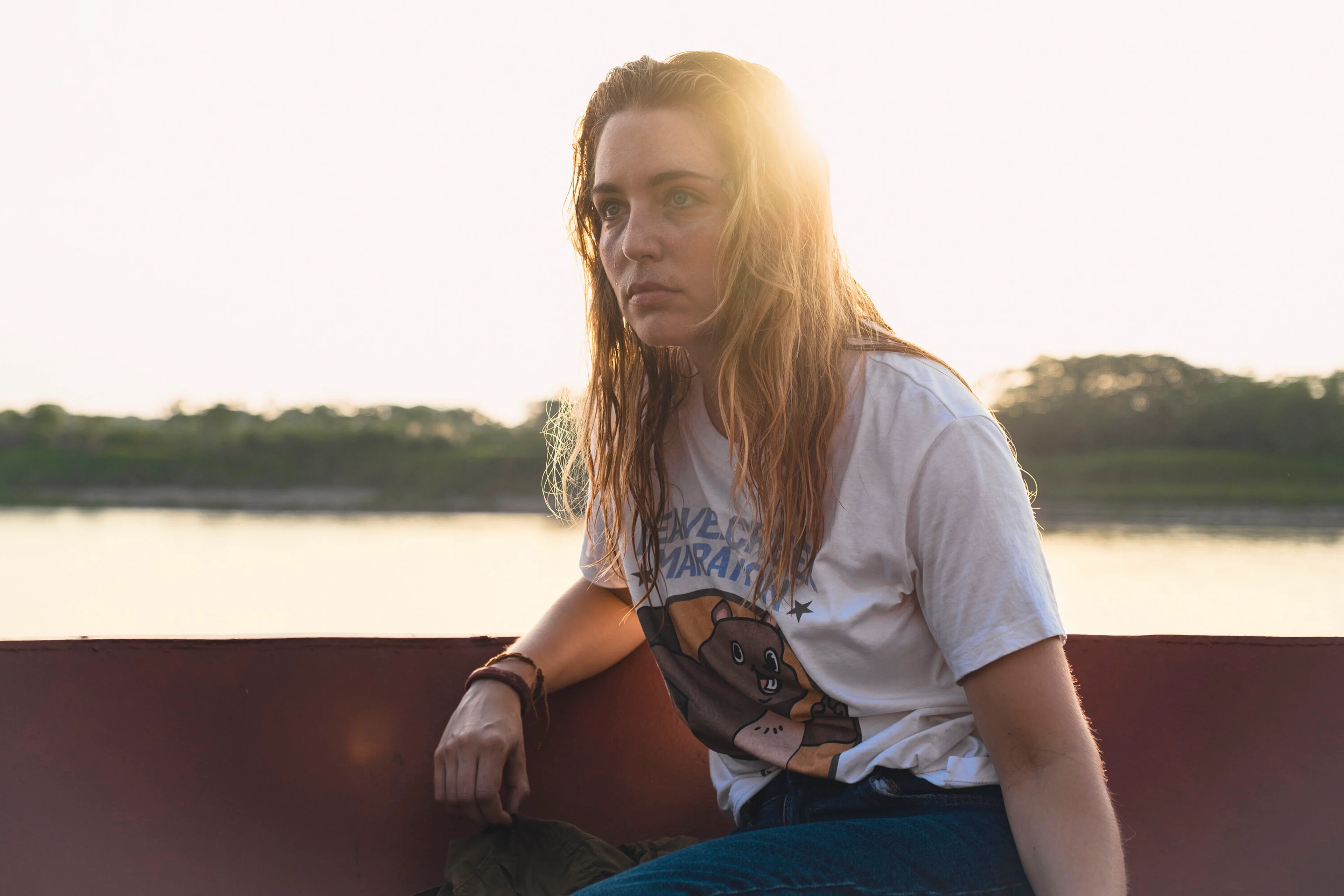 Jessica Rothe stands on a boat beside an Amazon river in a Beware Boiúna production still.