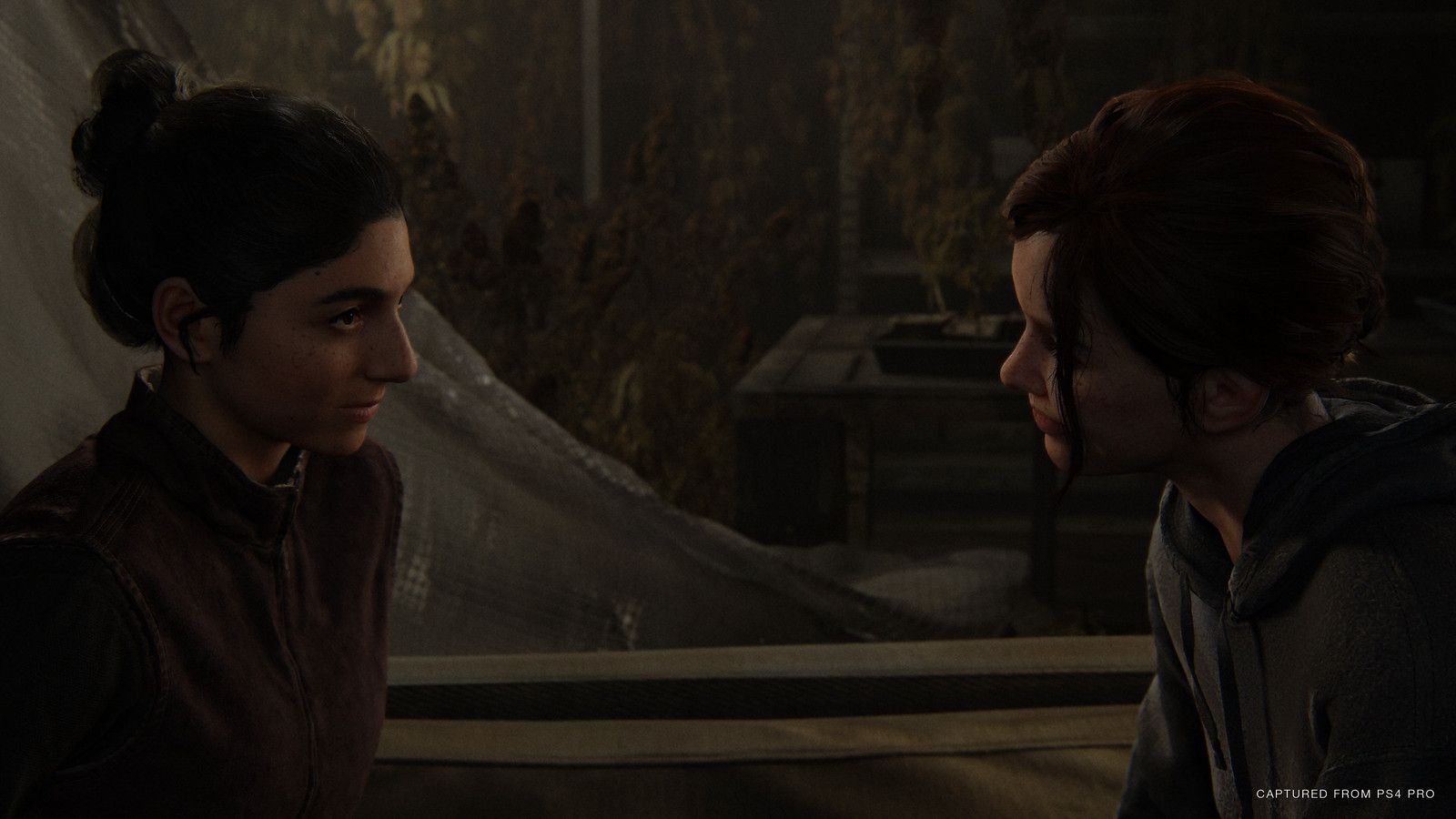 Dina and Ellie speak face to face in a quiet interior.