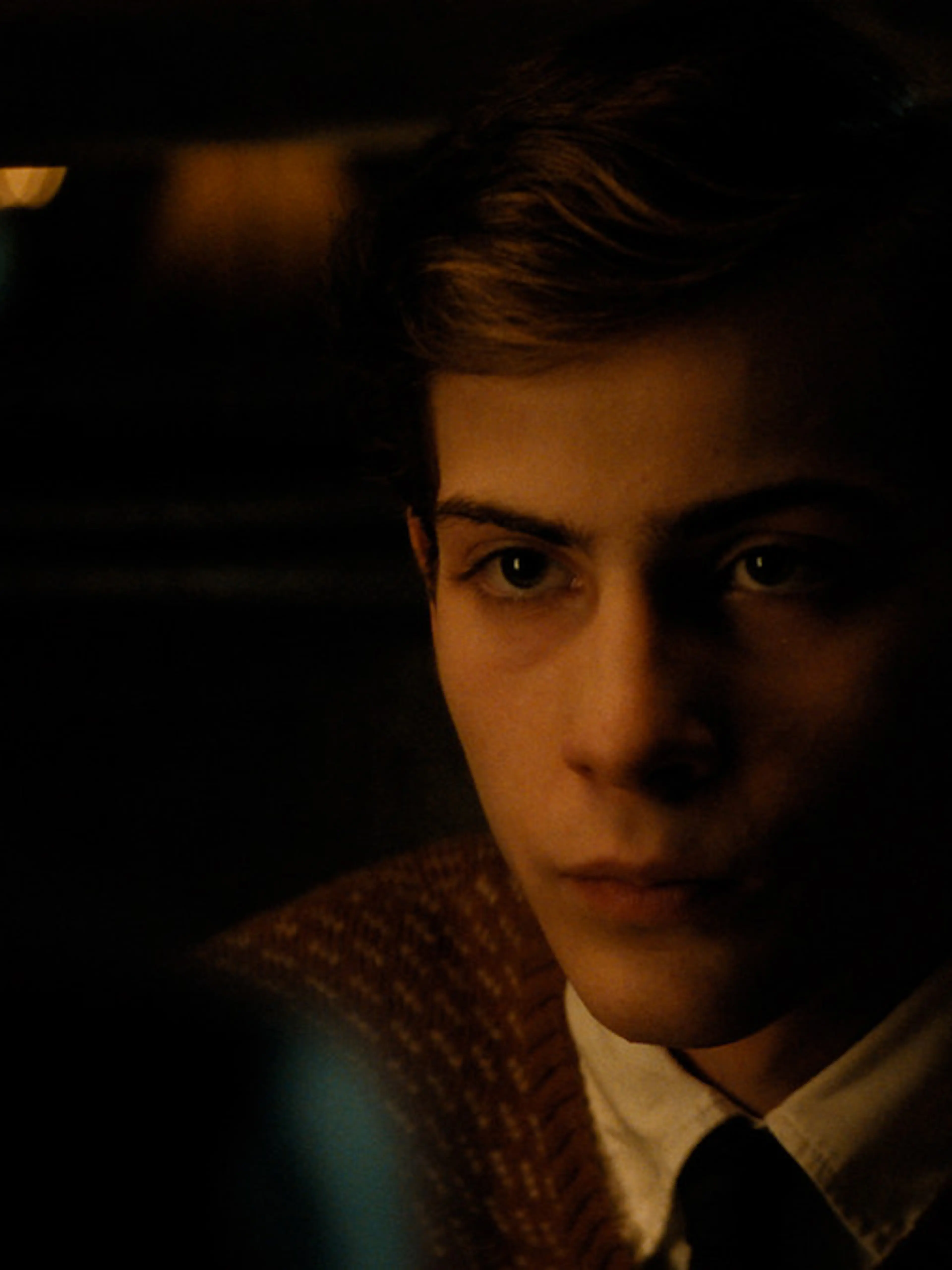 Jacob Tremblay as young Ted Kaczynski sits in a dimly lit scene from UNABOMBER.