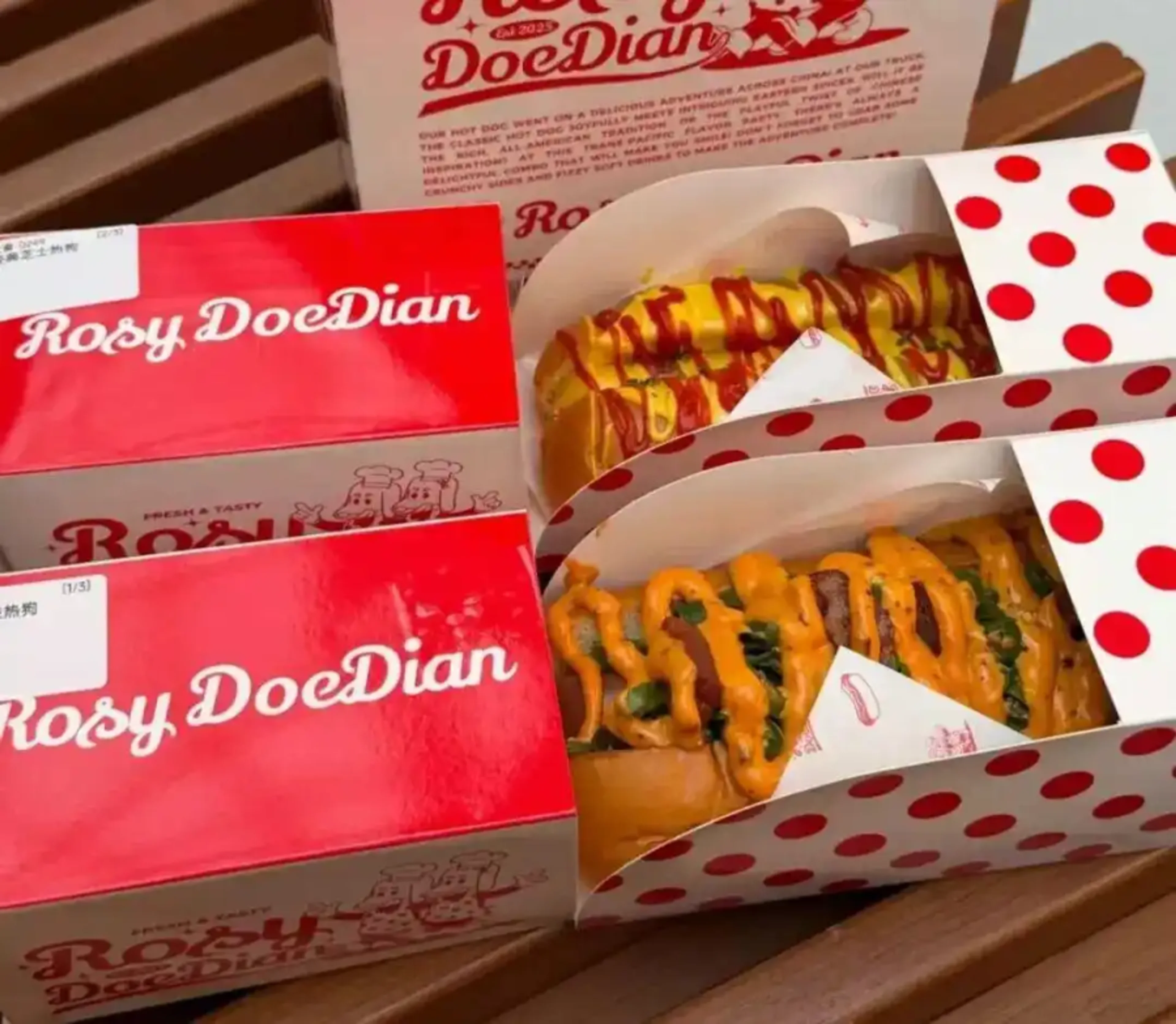 Two Rosy DoeDian hot dogs in red-and-white branded takeaway cartons.
