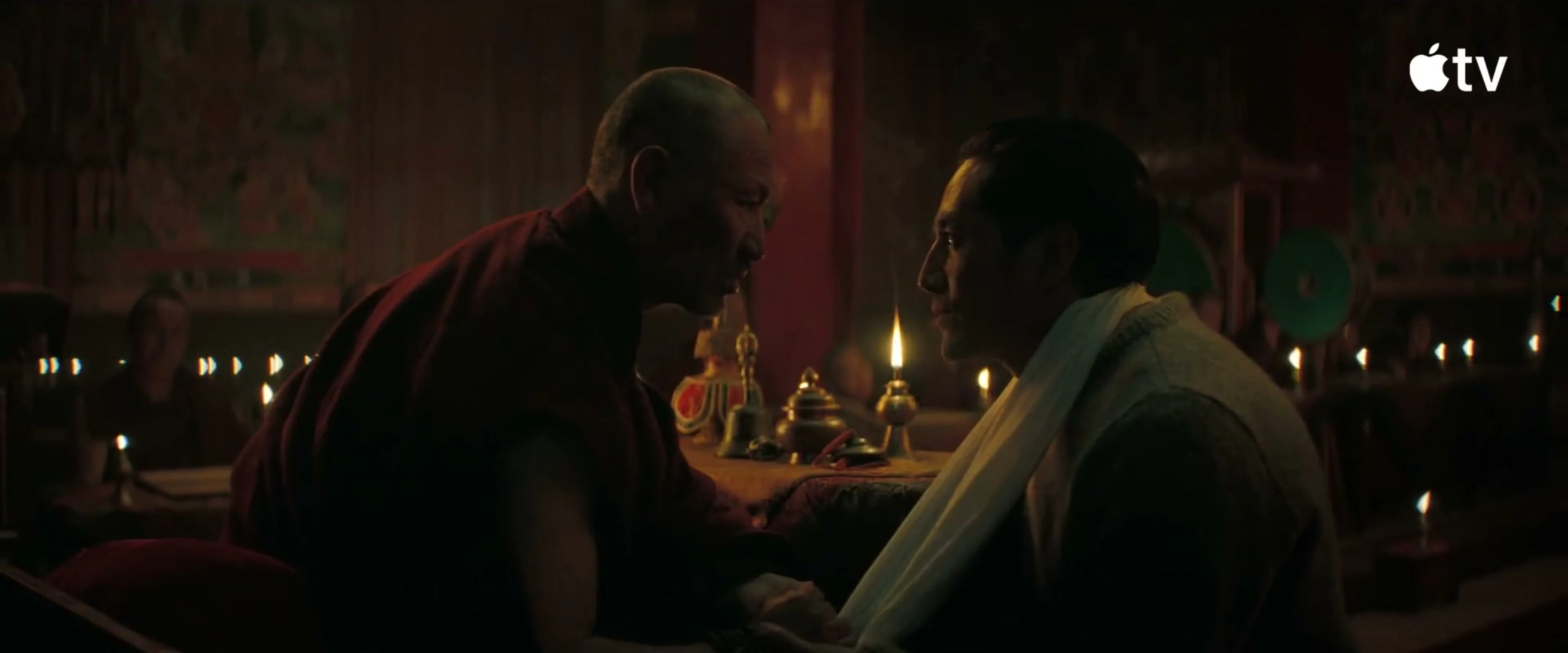 Tenzing speaks with a monk inside a candlelit temple.