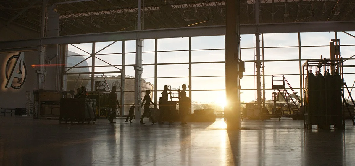 The remaining Avengers walk in silhouette across a sunlit hangar at Avengers Headquarters.